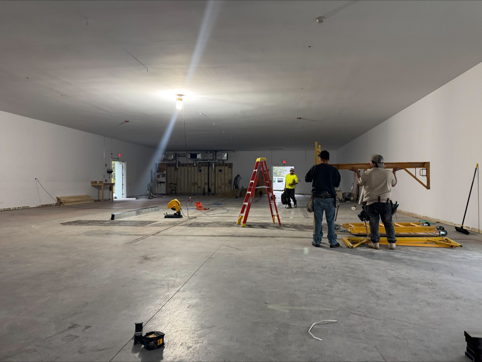 Workers and ladders inside a large empty warehouse under construction