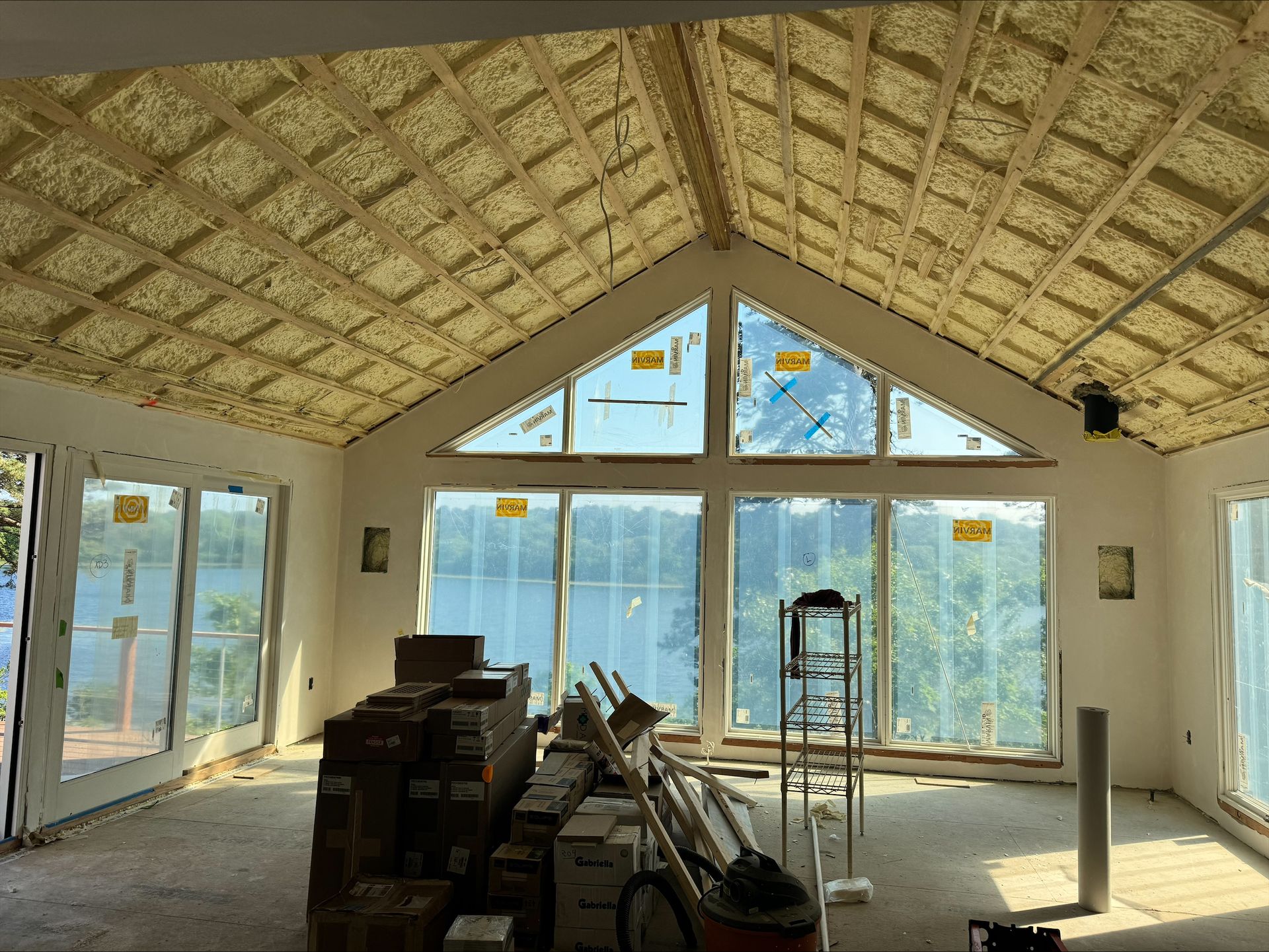 Partially furnished room with large windows, exposed ceiling, and construction materials inside