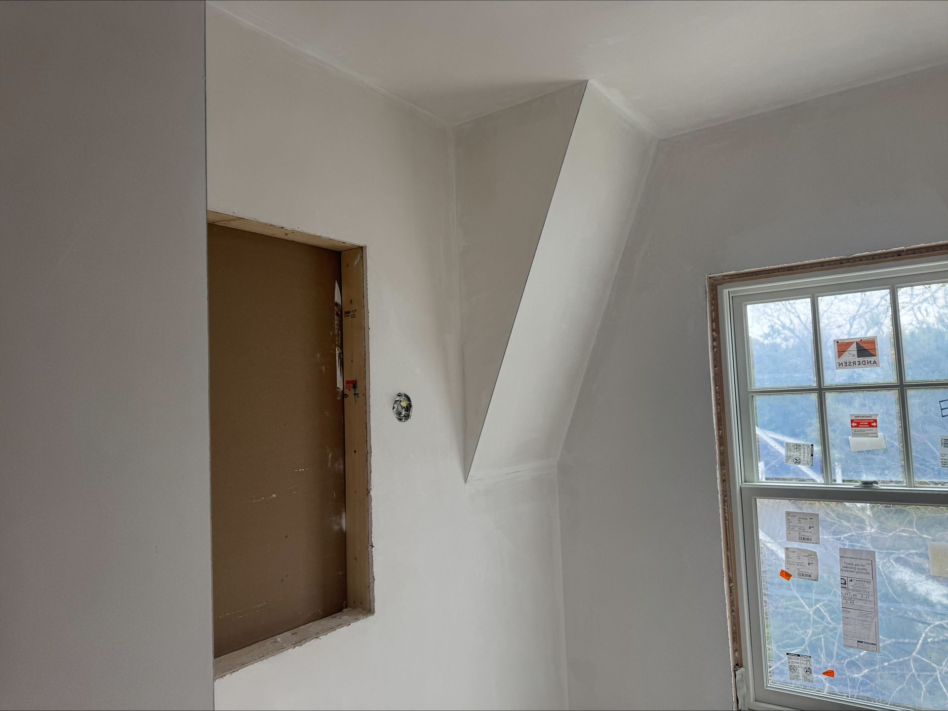 White interior wall with a recessed opening, slanted beam, and a window showing outdoor light.