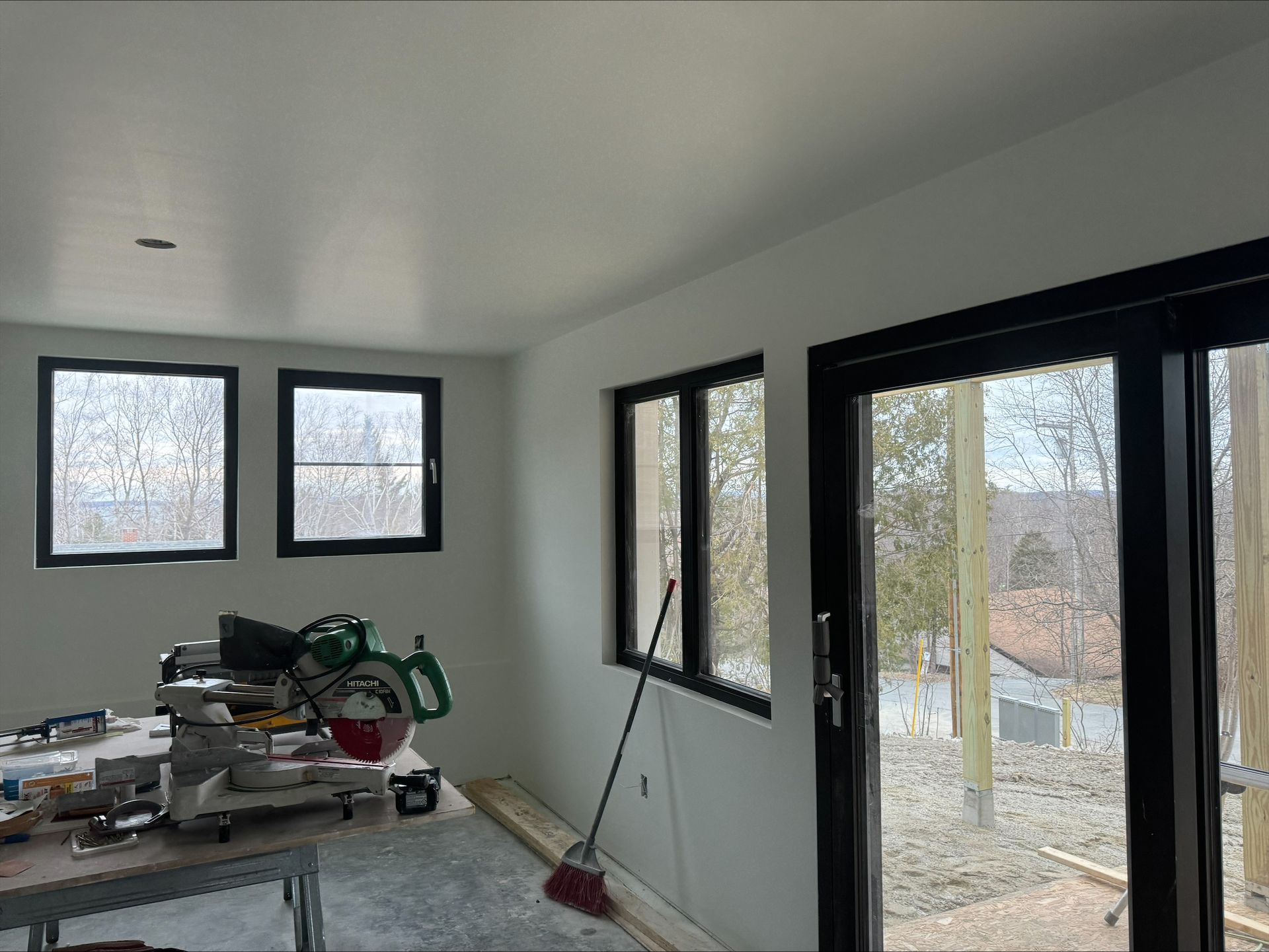 Unfinished room with white walls, windows, a glass door, and construction materials piled on the floor.