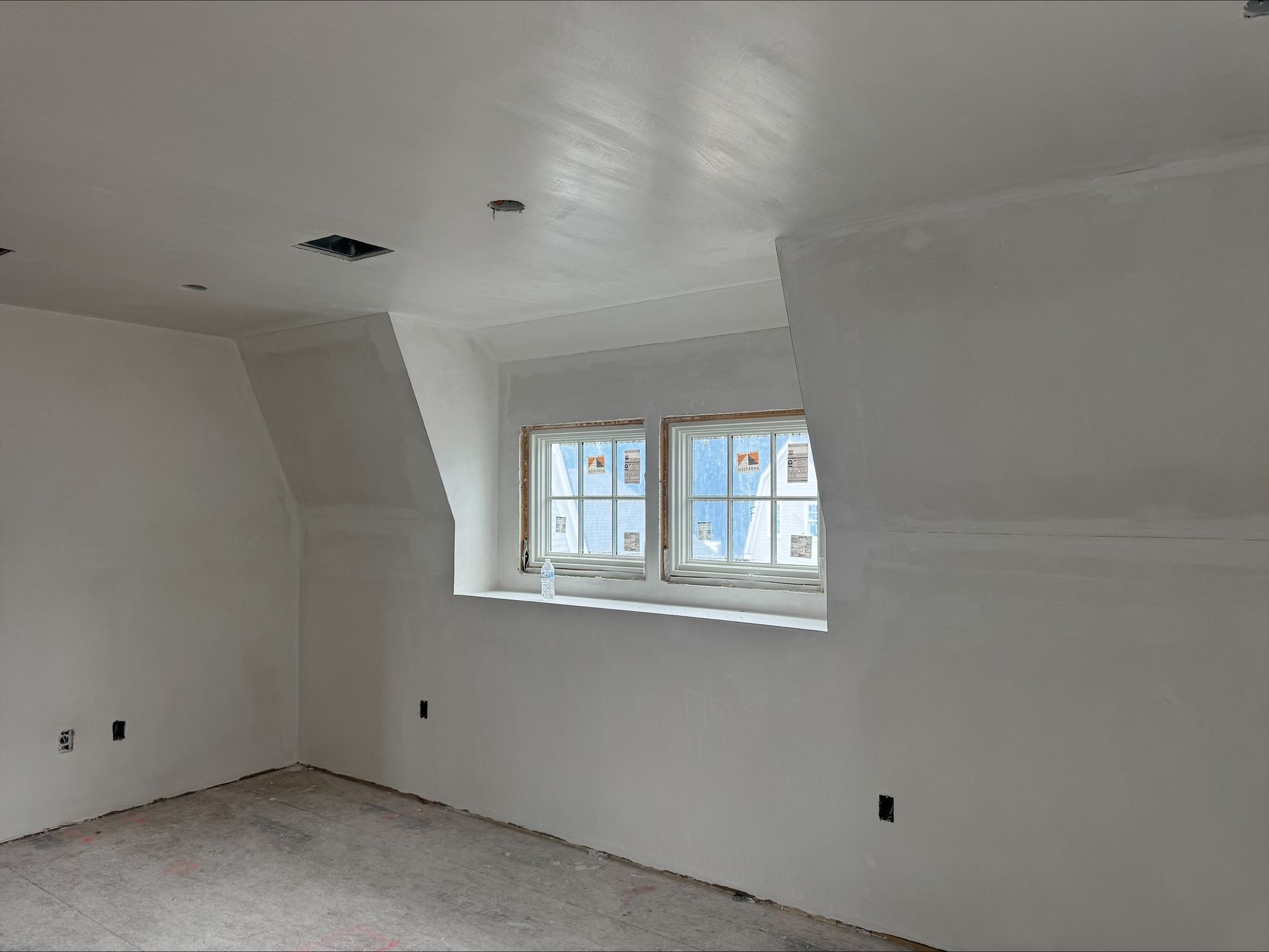 Empty white room with sloped ceiling, bare floor, and a small window on the right wall