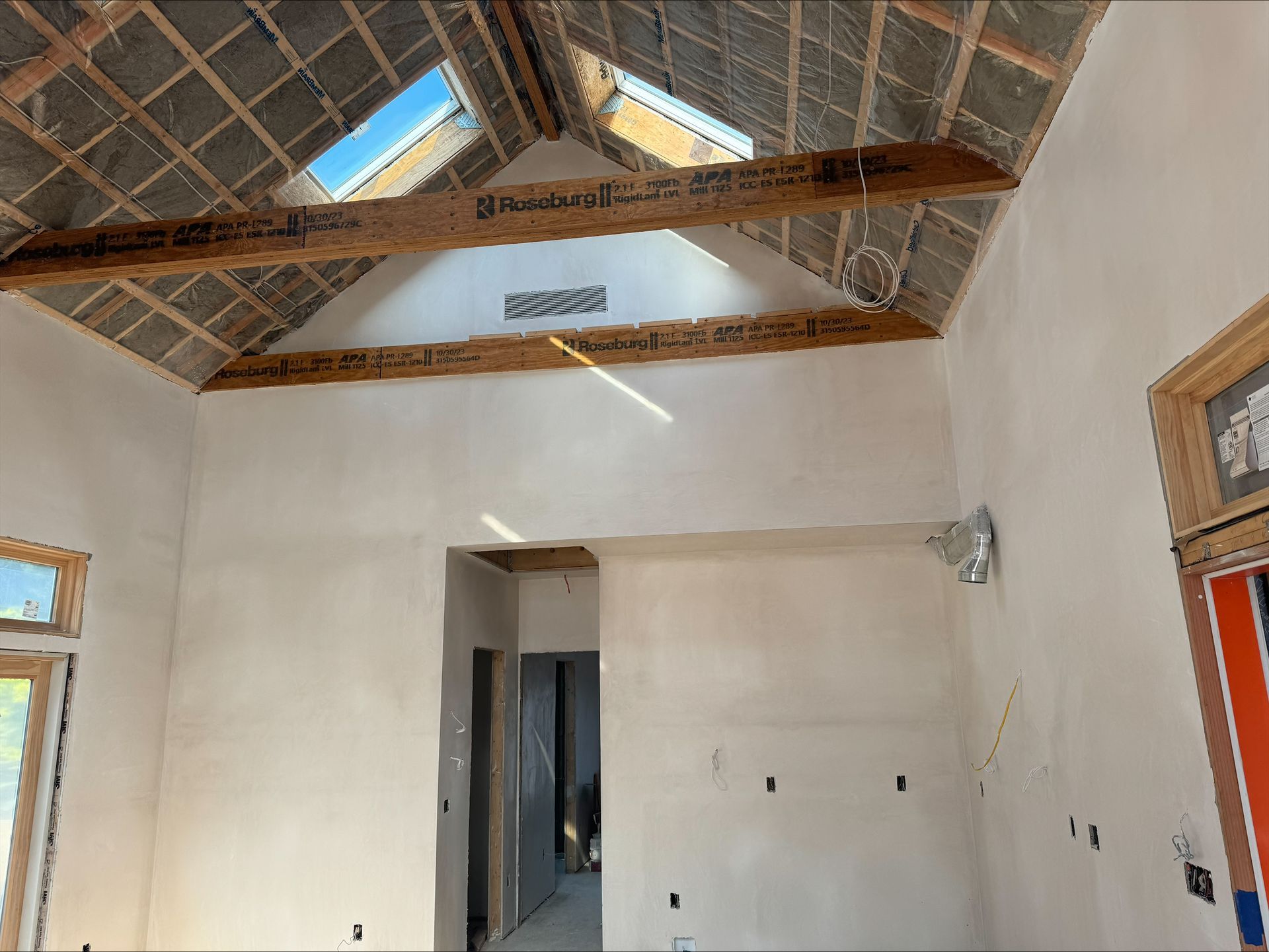 Unfinished room with white walls, exposed rafters, and a partially vaulted wood-and-tin ceiling.