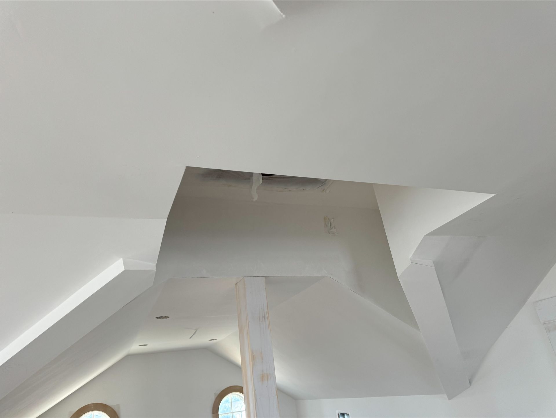Ceiling vent and ductwork in a white interior room, with exposed structural beams.