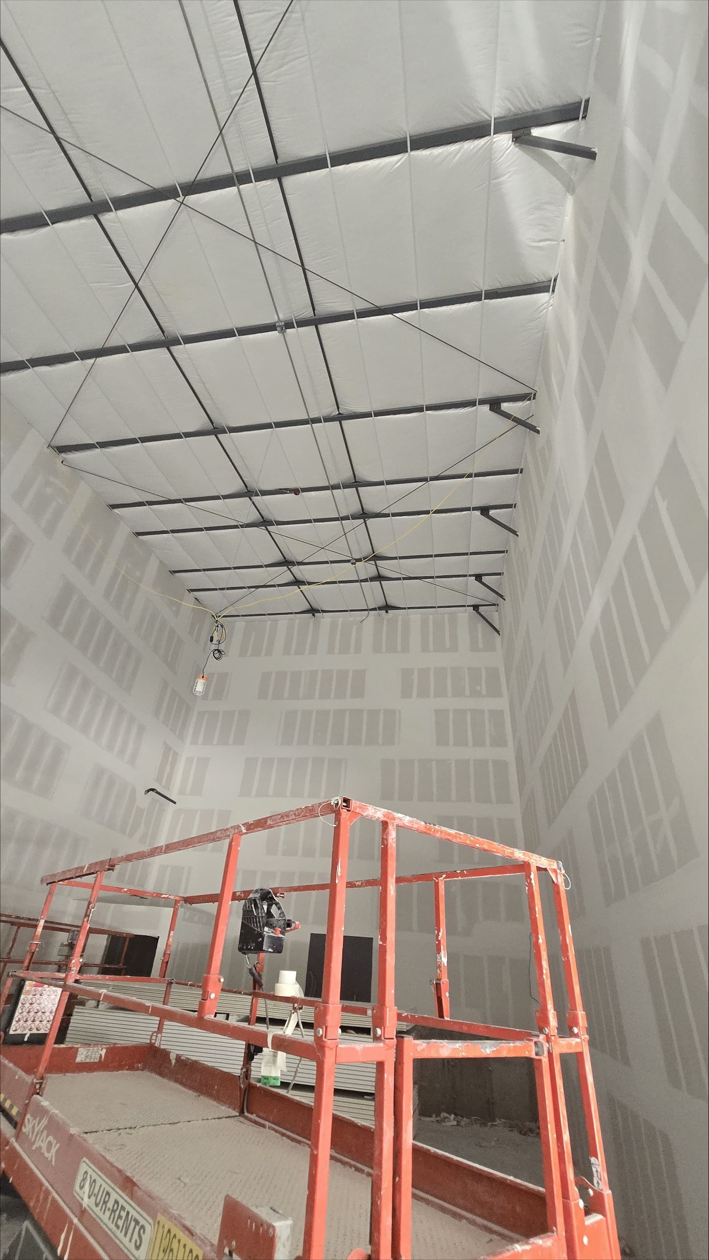 Construction lift inside a large industrial room with suspended cables and white patterned walls