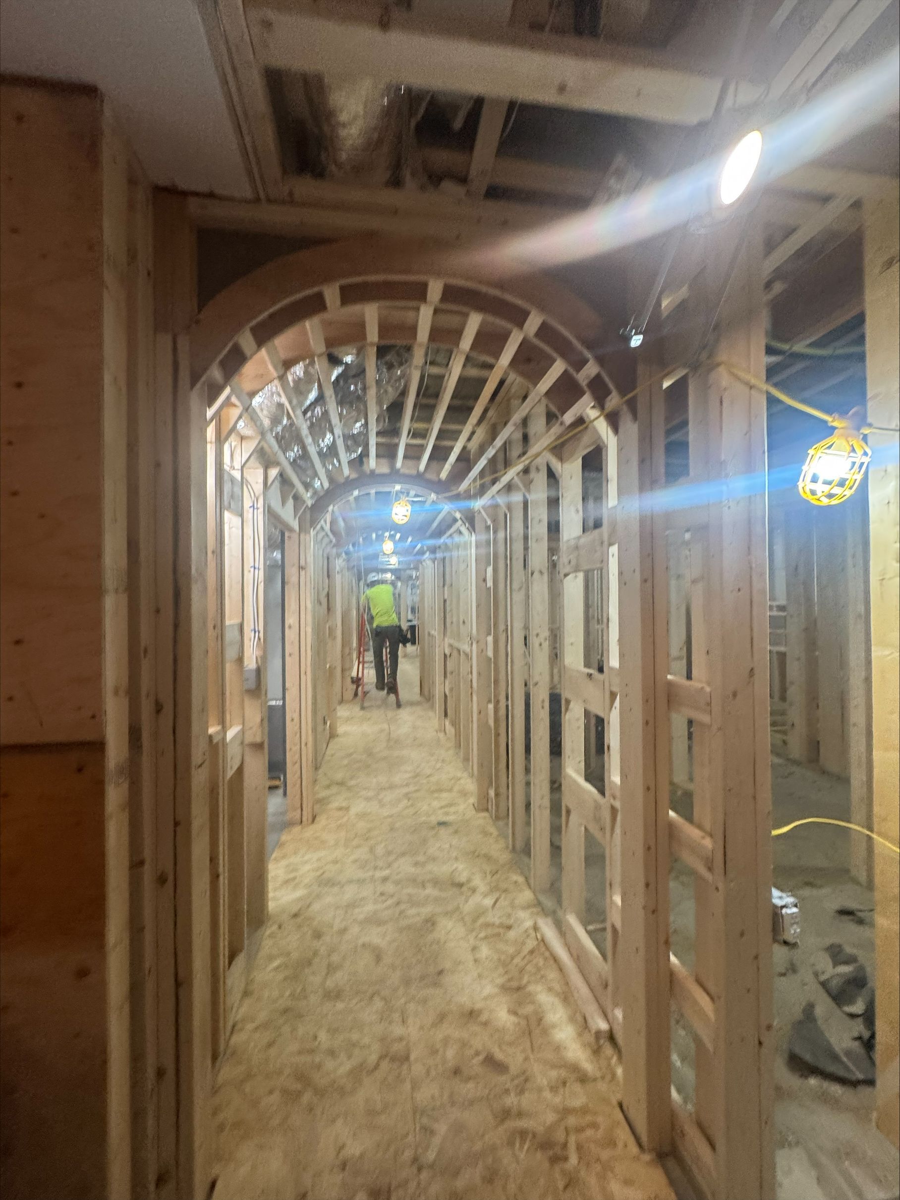 Framed hallway under construction with wood studs, arched ceiling supports, and a dusty floor