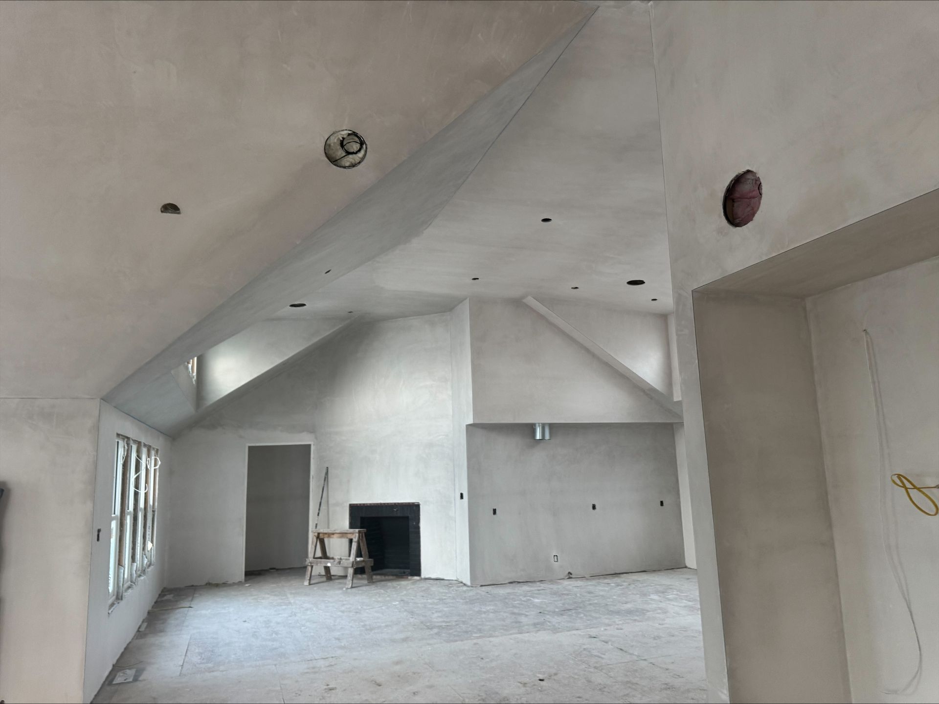 Empty unfinished room with vaulted ceiling, white walls, large windows, and a fireplace alcove