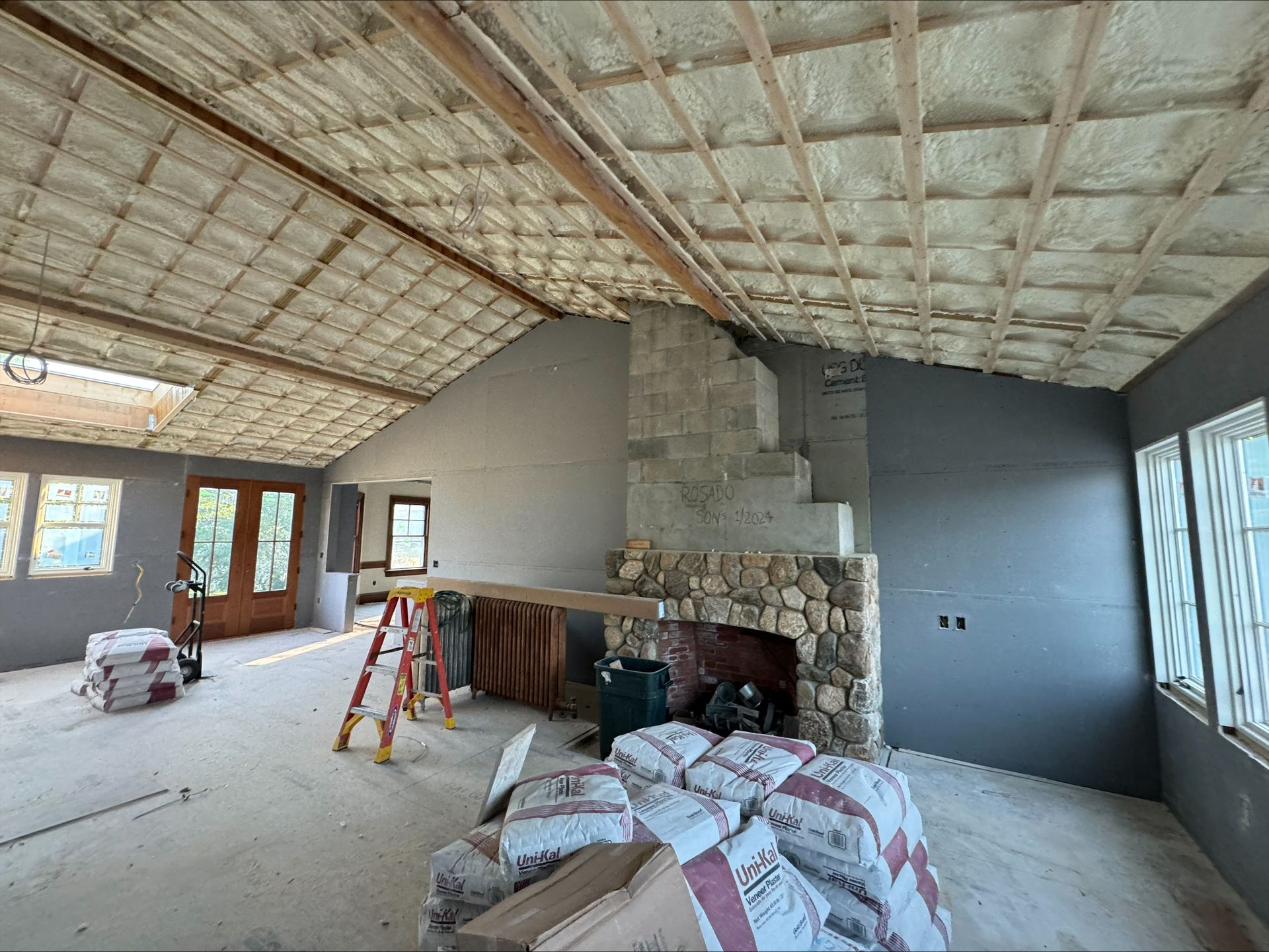 Partially renovated room with exposed ceiling, stone fireplace, ladder, and construction materials