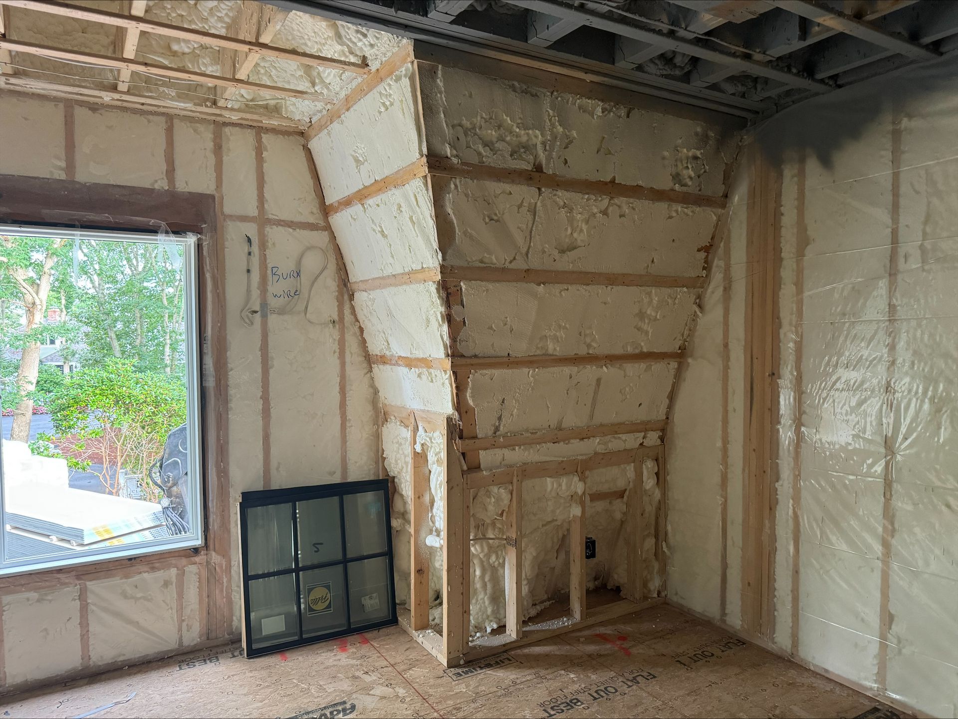 Interior under construction with insulated walls, exposed framing, and a window view outside.