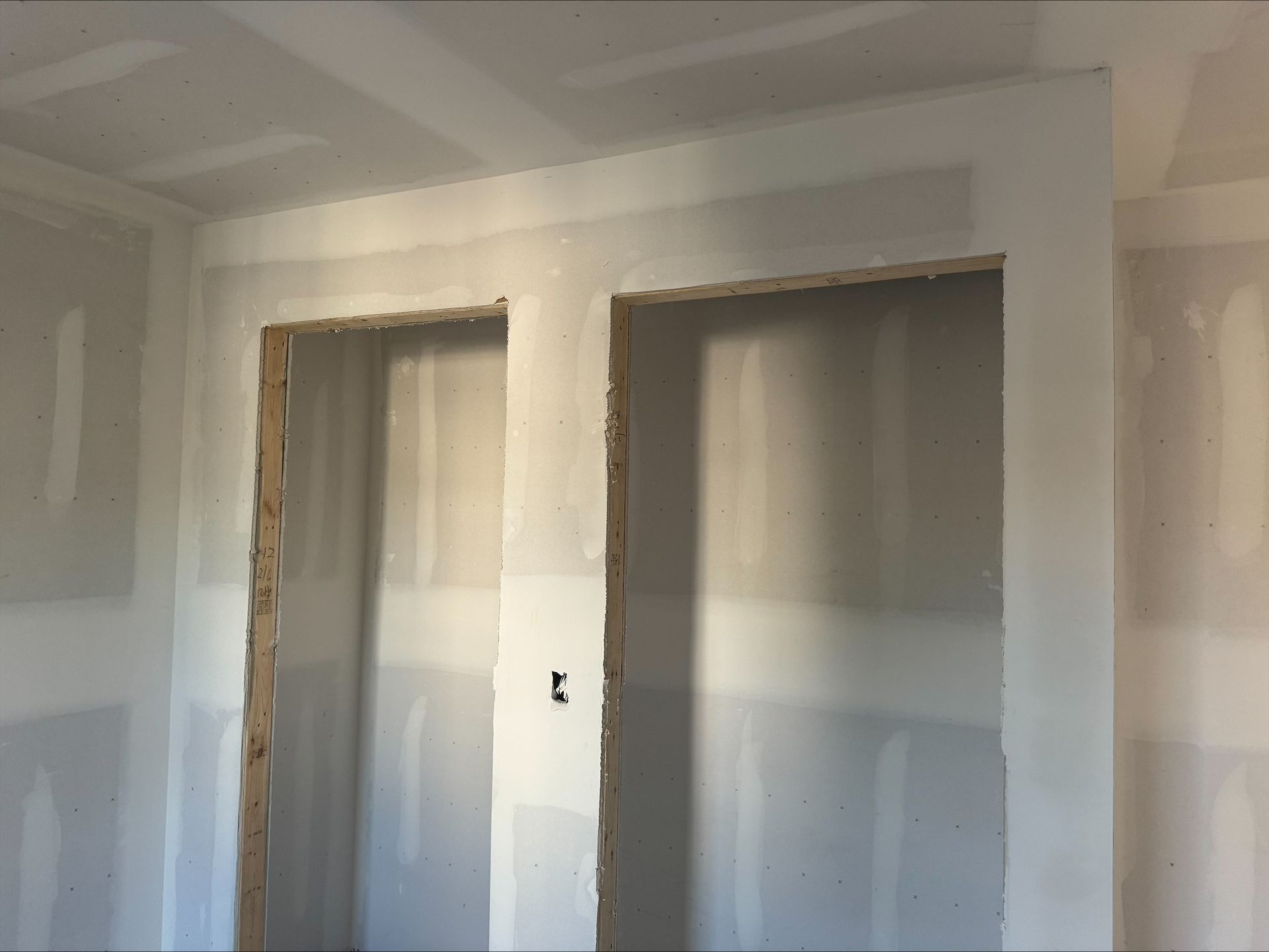Unfinished interior room with drywall seams and two door openings outlined in wood.