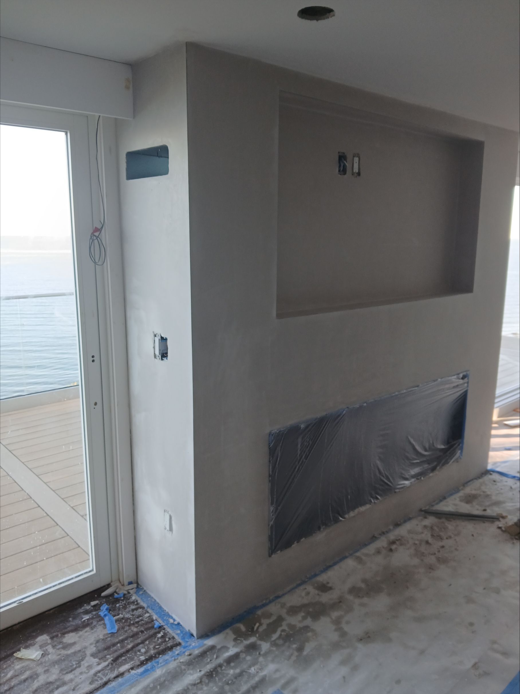 Unfinished gray wall with built-in alcoves beside a bright sliding glass door on a balcony.