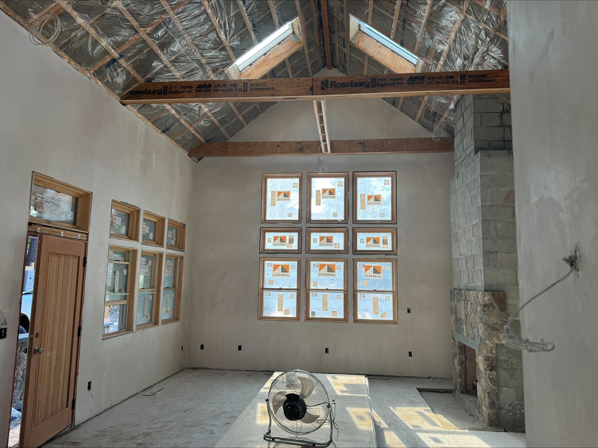 Partially finished room with exposed ceiling beams, windows, and a central floor hole for construction work