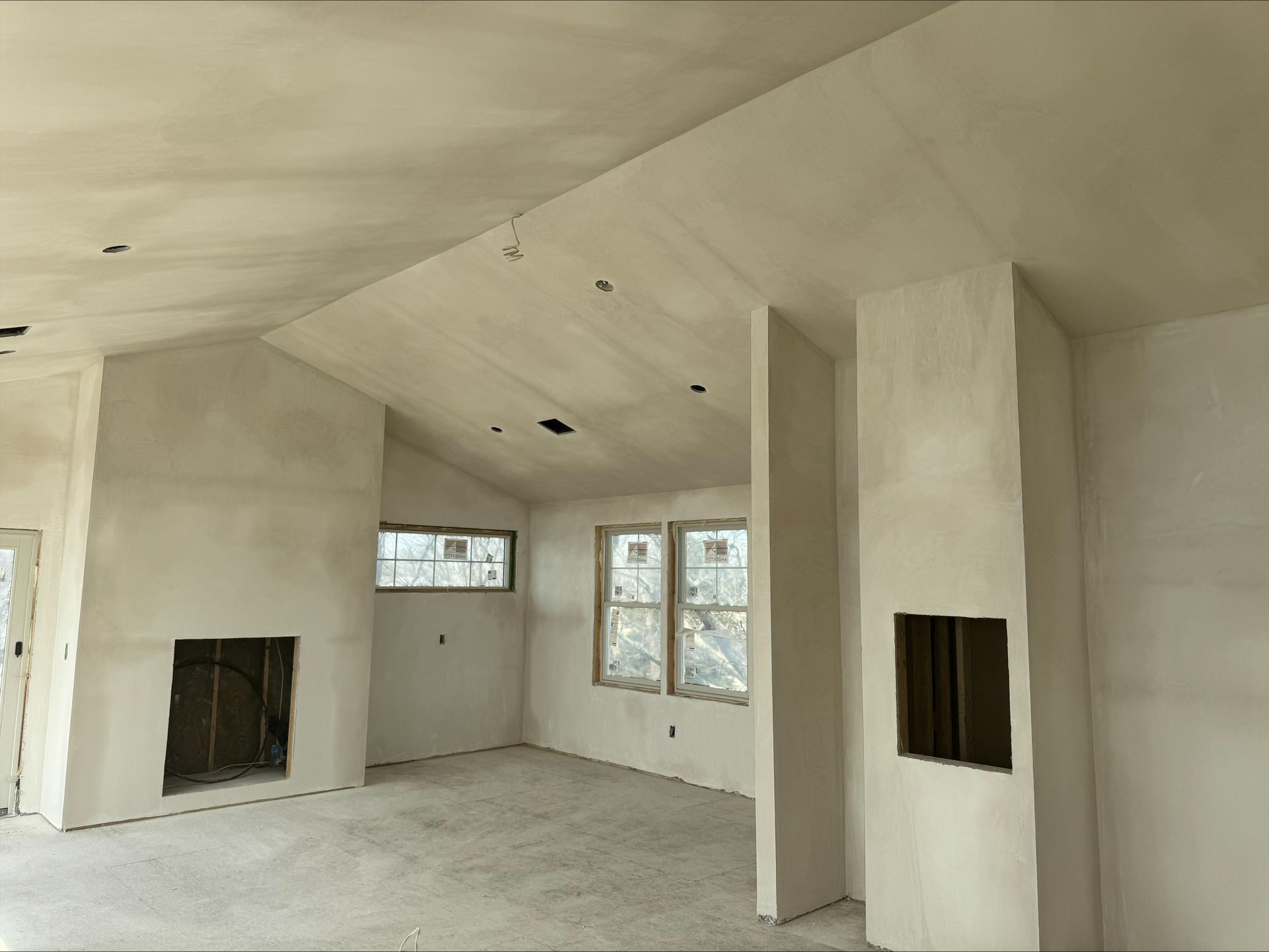 Unfinished white living room with fireplace, windows, and exposed sloped ceiling under construction