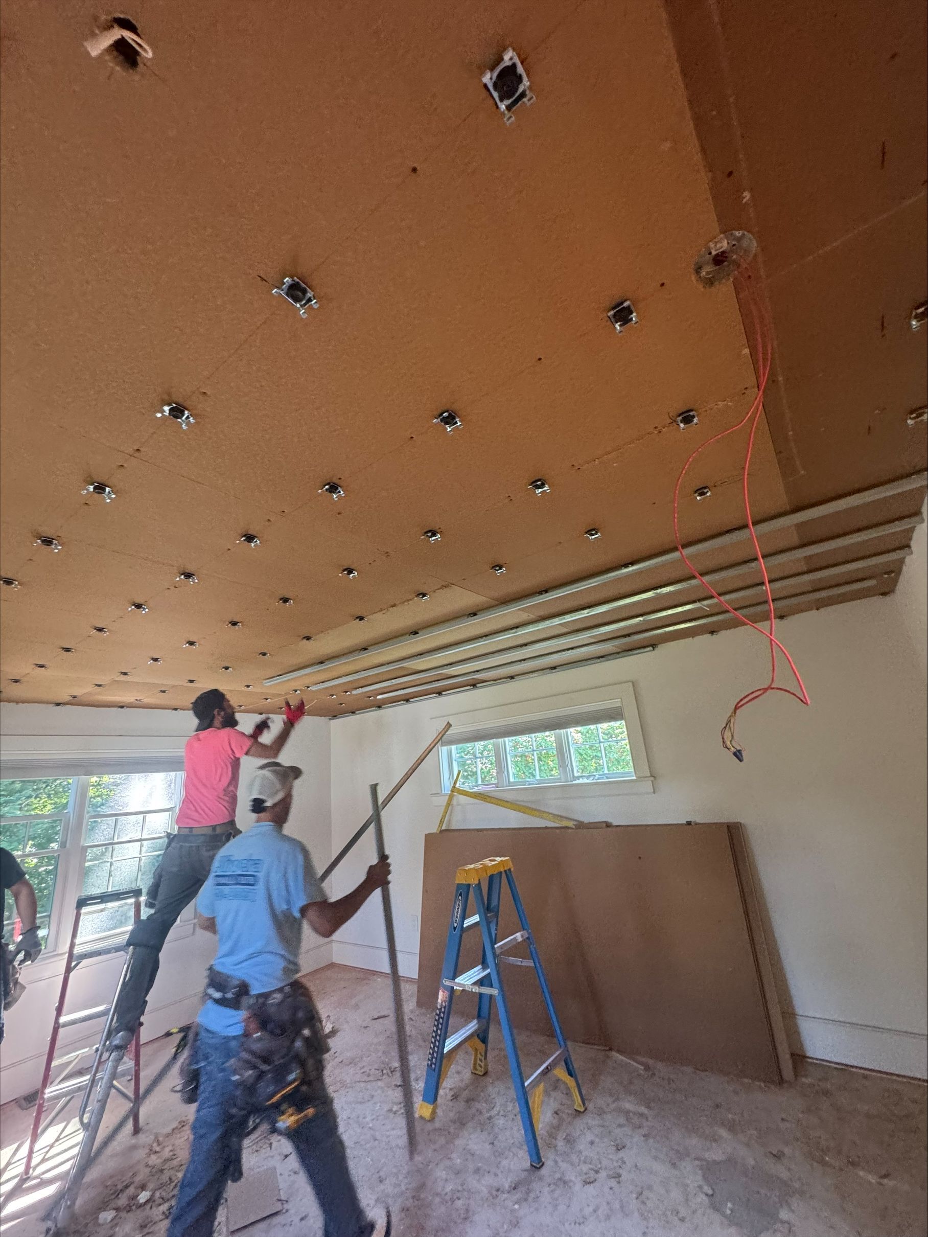Workers installing ceiling panels in a room with ladders and tools.