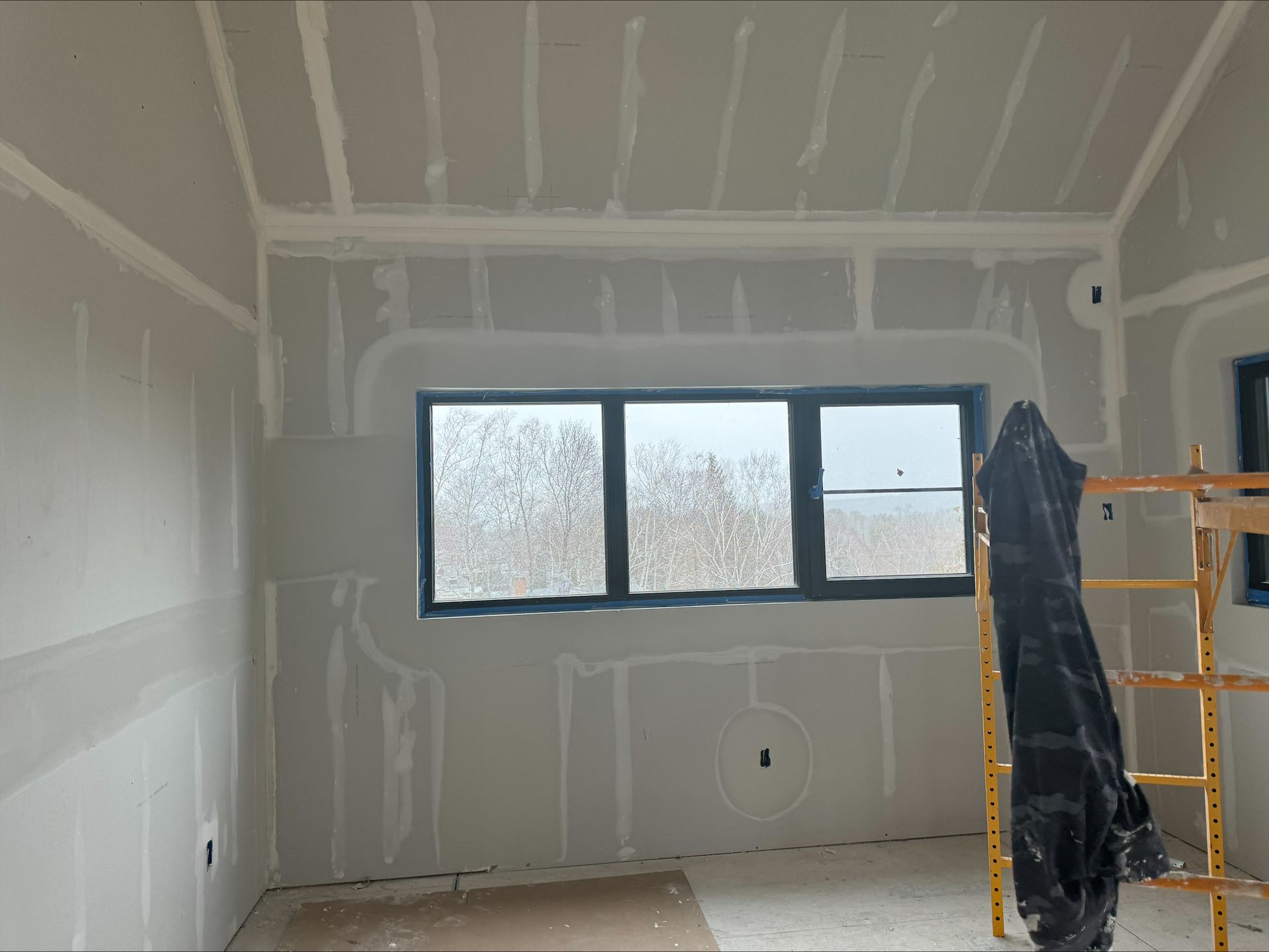 Partially finished room with drywall, a black-framed window, and scaffolding on the right.