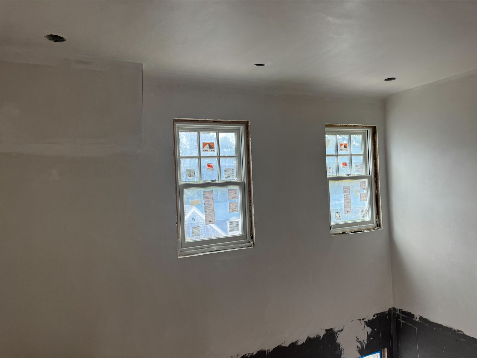 Empty white room with two small windows and unfinished dark paint along the lower walls