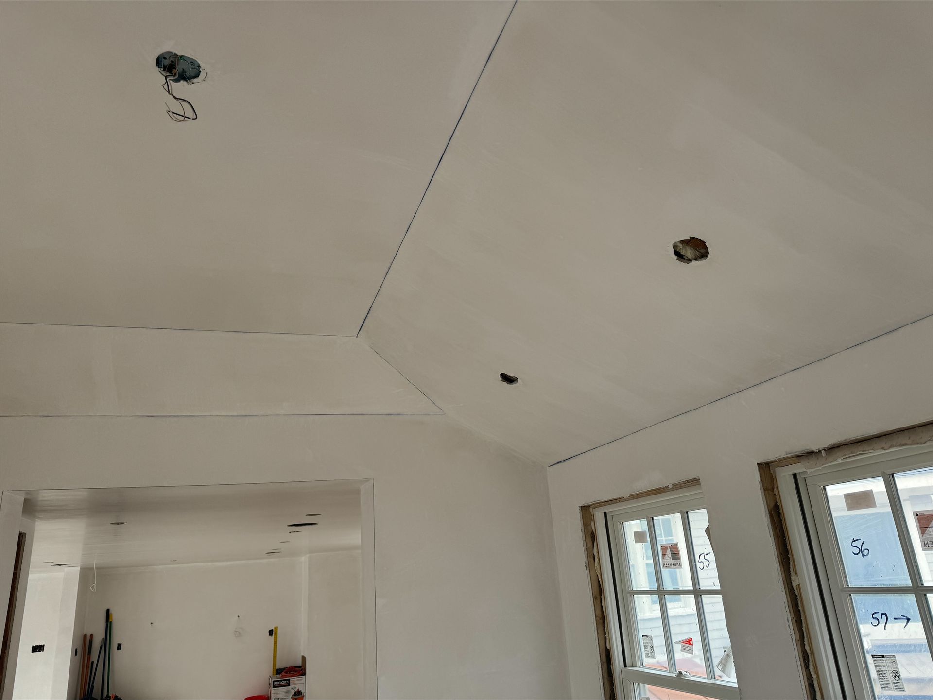 White room interior with a sloped ceiling, unfinished light fixtures, and windows on the right.