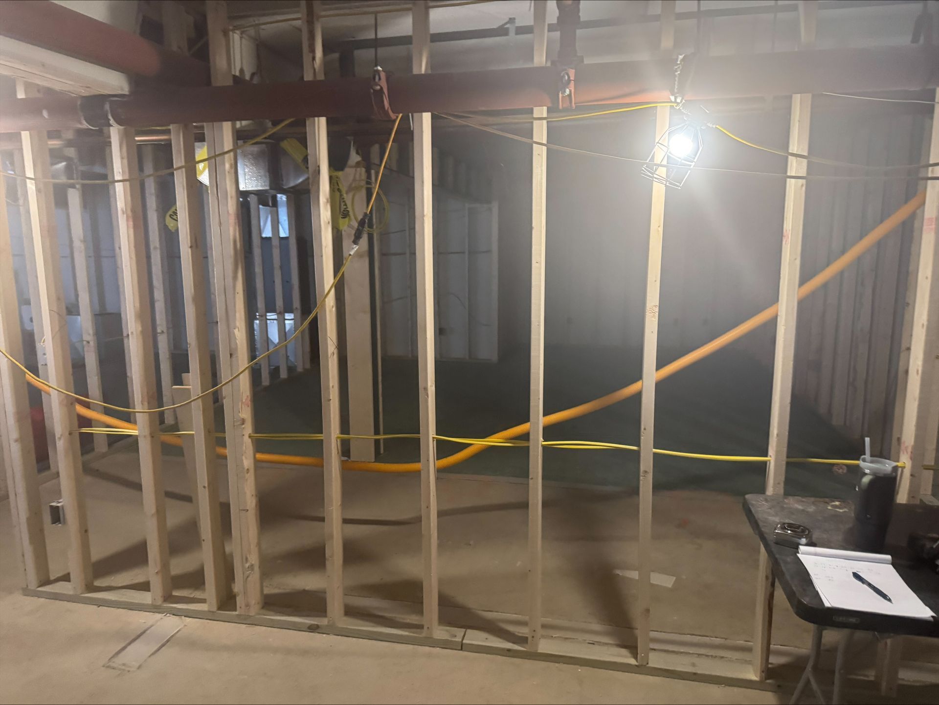 Wood-framed interior under construction with exposed studs, insulation, and bright work lights.