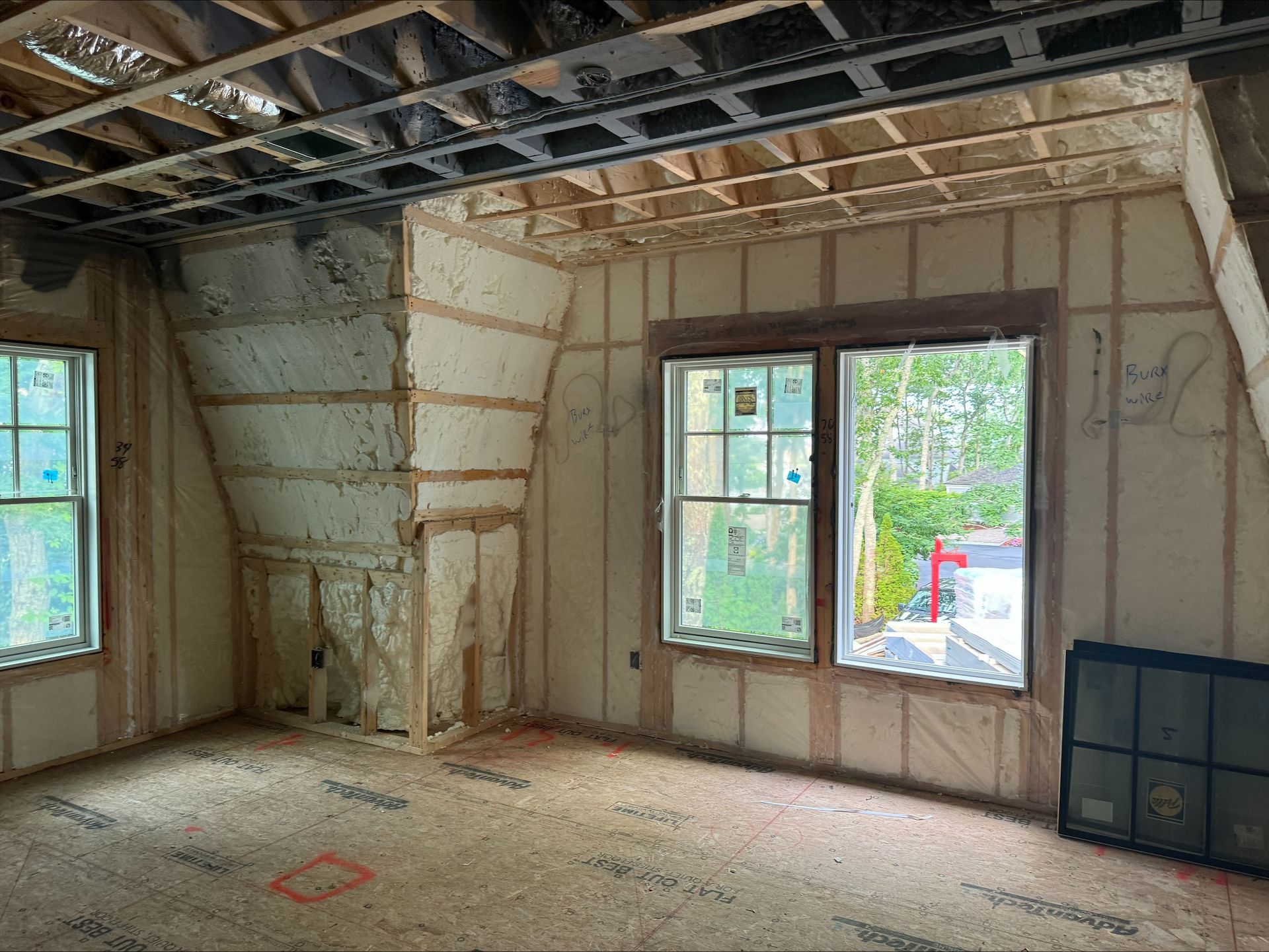 Unfinished room with exposed framing, insulated walls, windows, and debris on the floor