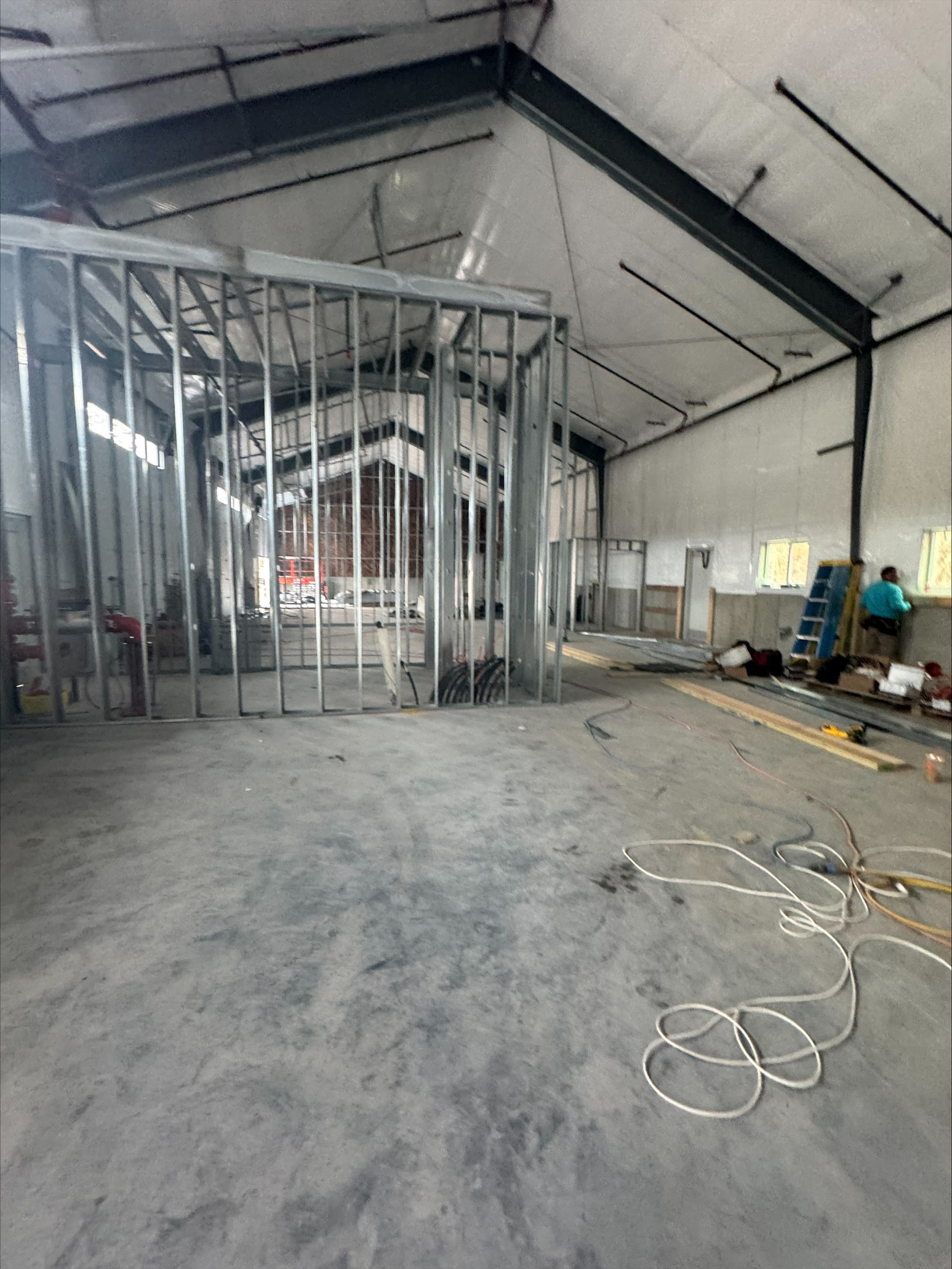Interior of an unfinished warehouse with metal framing, exposed roof, and construction materials on the floor