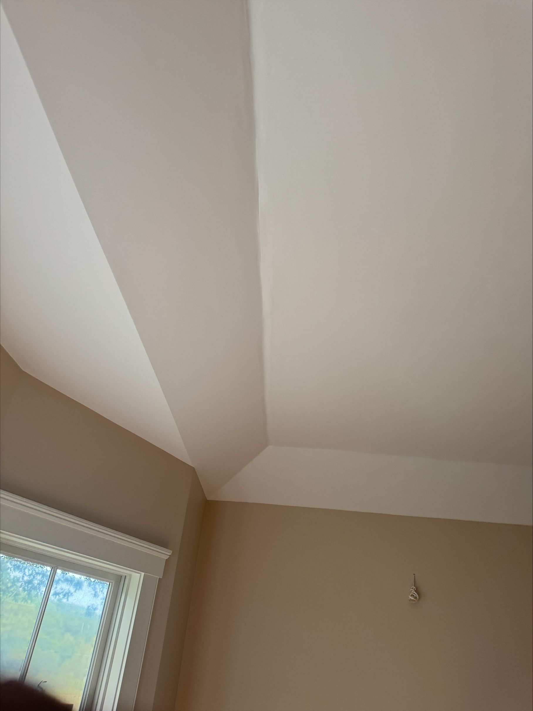 Corner of a room with beige walls, white ceiling beams, and a window letting in daylight