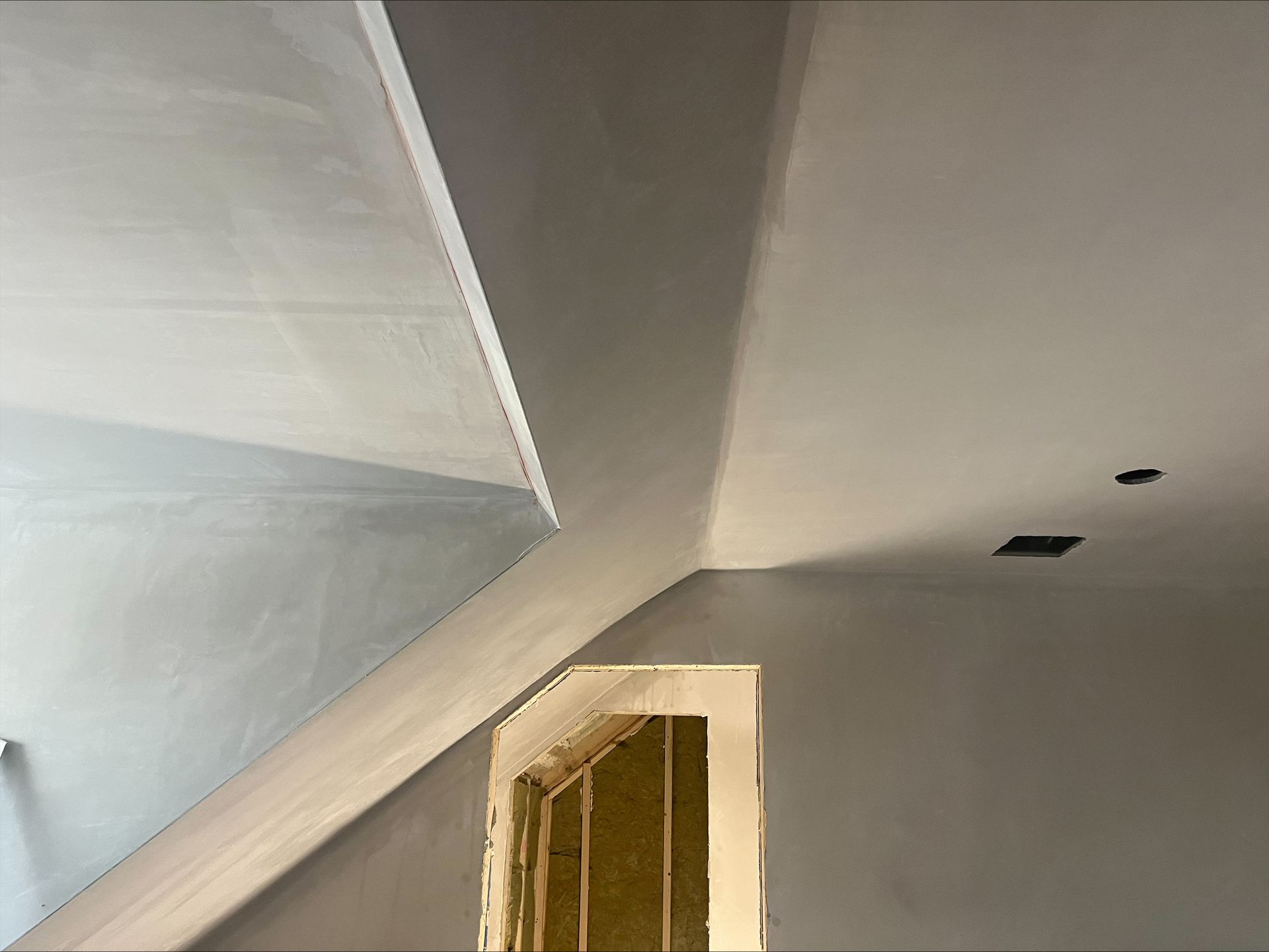 White slanted ceiling above a doorway in an unfinished room with patchy paint and two small wall holes