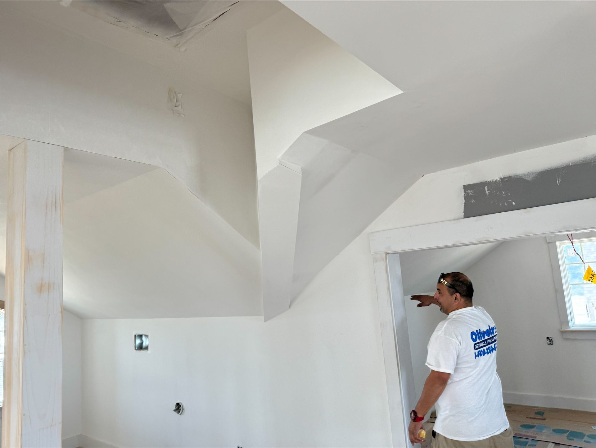 Man standing in a white room with unfinished ceiling and walls, inspecting the interior.