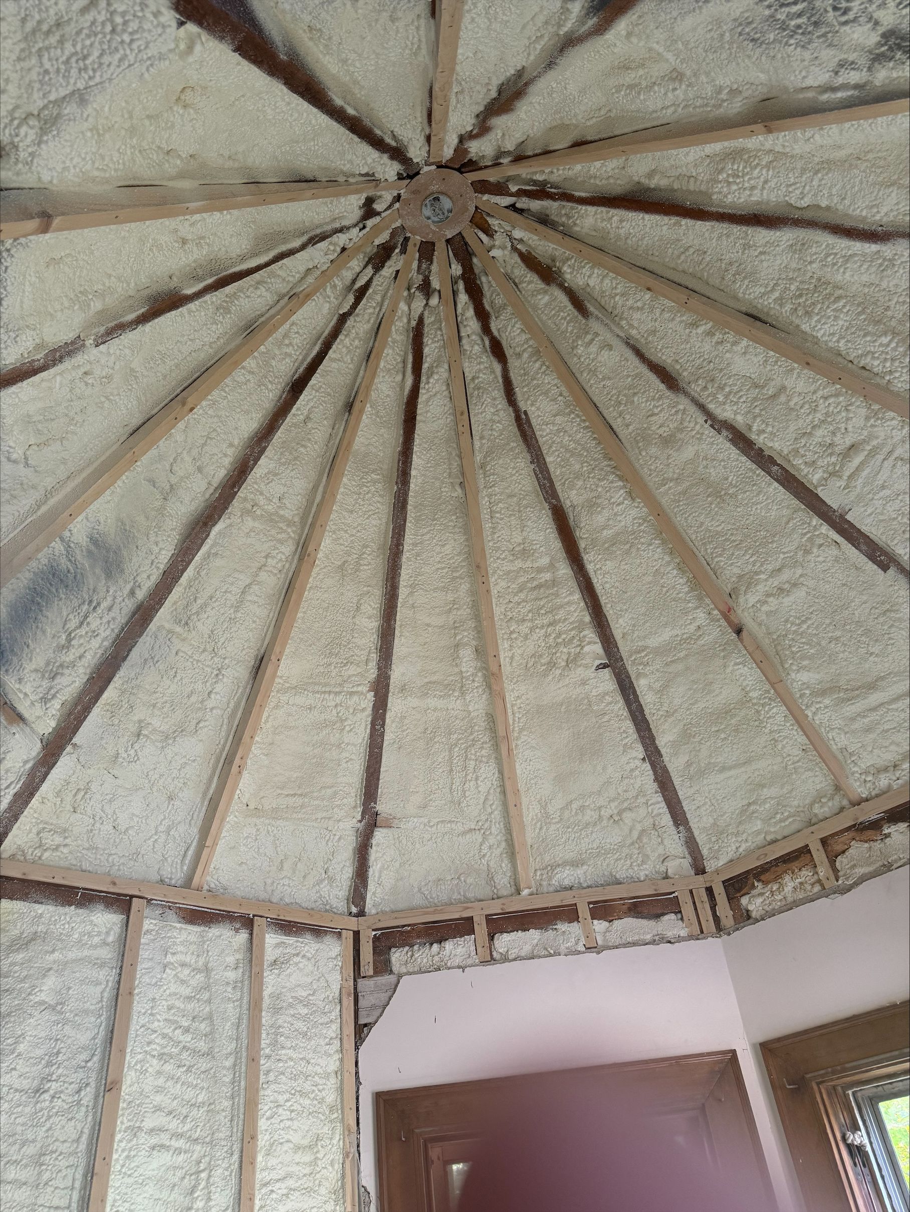 Interior of a round thatched ceiling with wooden beams above a room and window