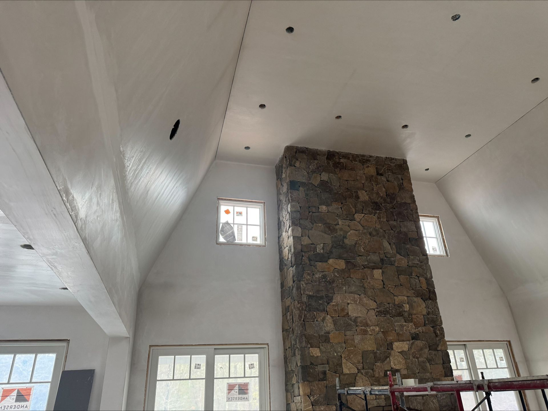 Interior with a tall stone fireplace centered in a white vaulted room with small windows.