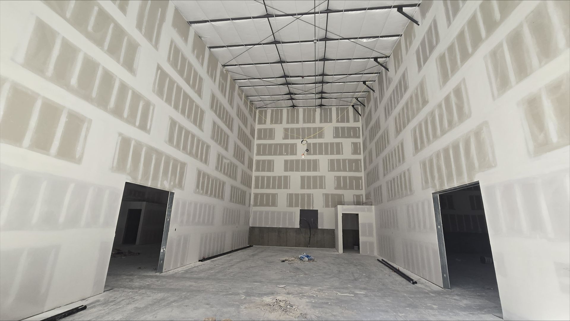 Empty unfinished room with drywall, exposed ceiling framing, and two open doorways on either side.