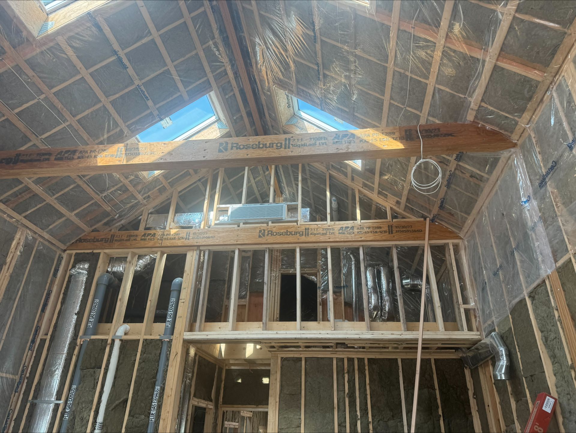 Interior of unfinished wooden building with exposed rafters, insulation, and framing under a peaked roof.