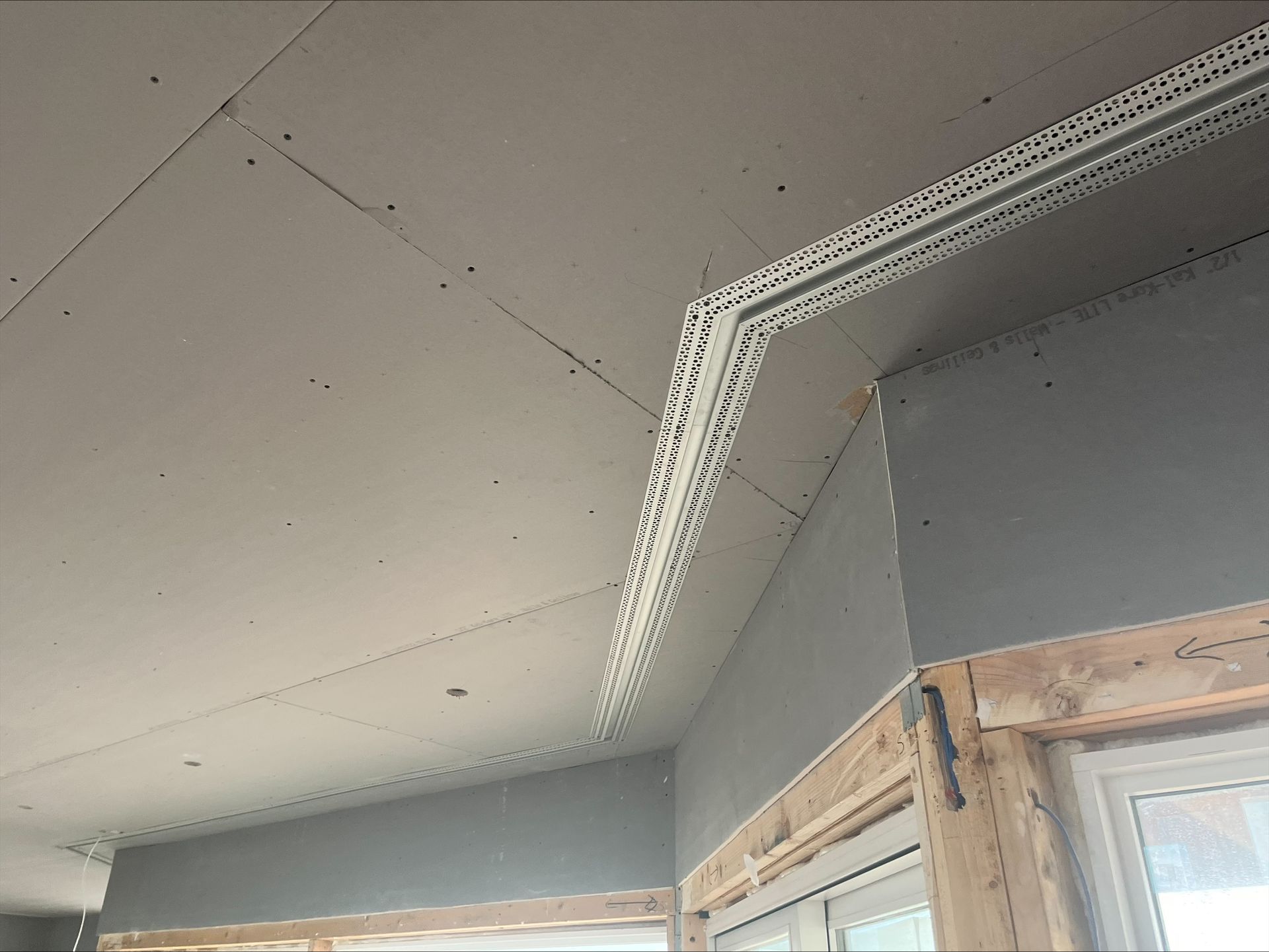 Corner of a room with a white perforated ceiling vent strip and gray walls above a window frame