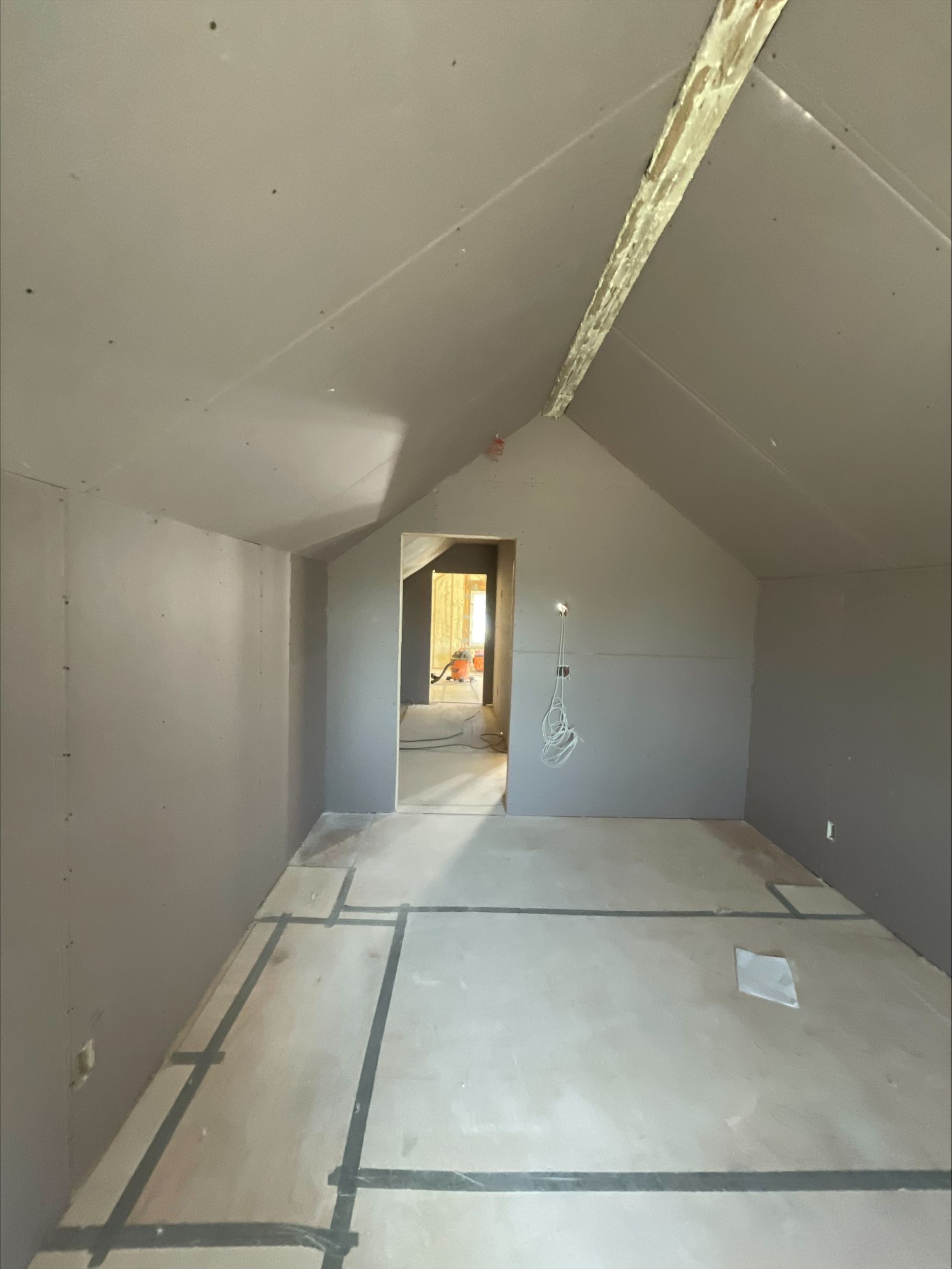 Unfinished attic room with sloped ceiling, drywall seams, and a doorway at the far end.