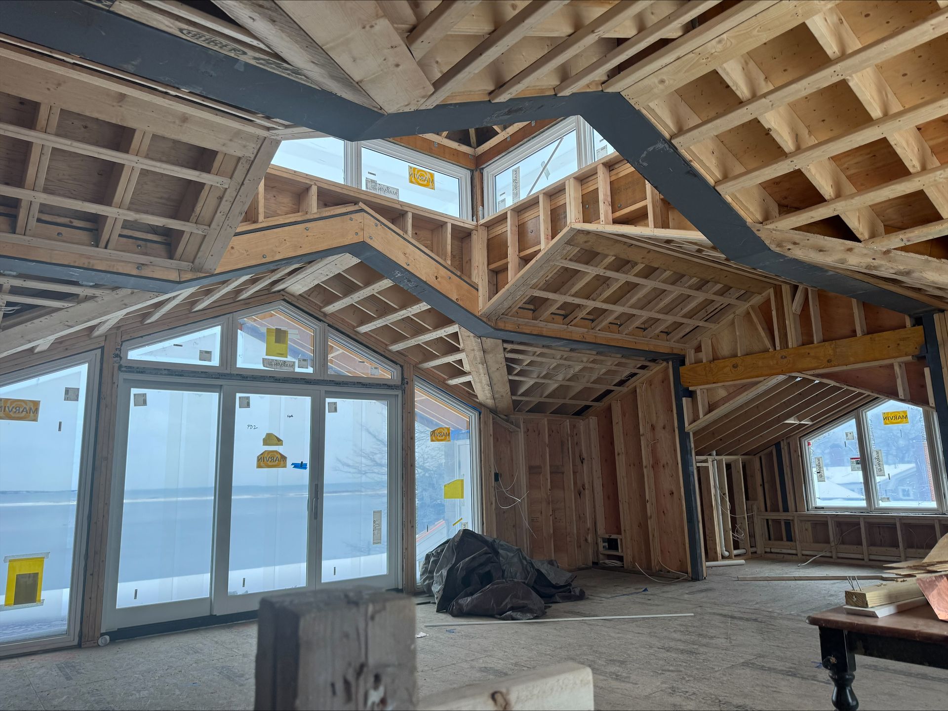 Unfinished room with exposed wooden roof framing, large windows, and a concrete floor under construction.