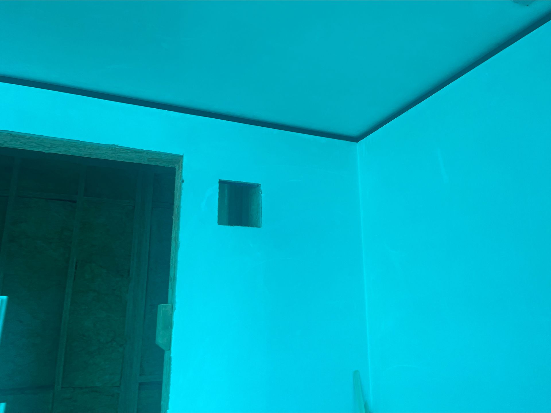 Blue-tinted room interior with a doorway, plain walls, and a small square opening near the ceiling