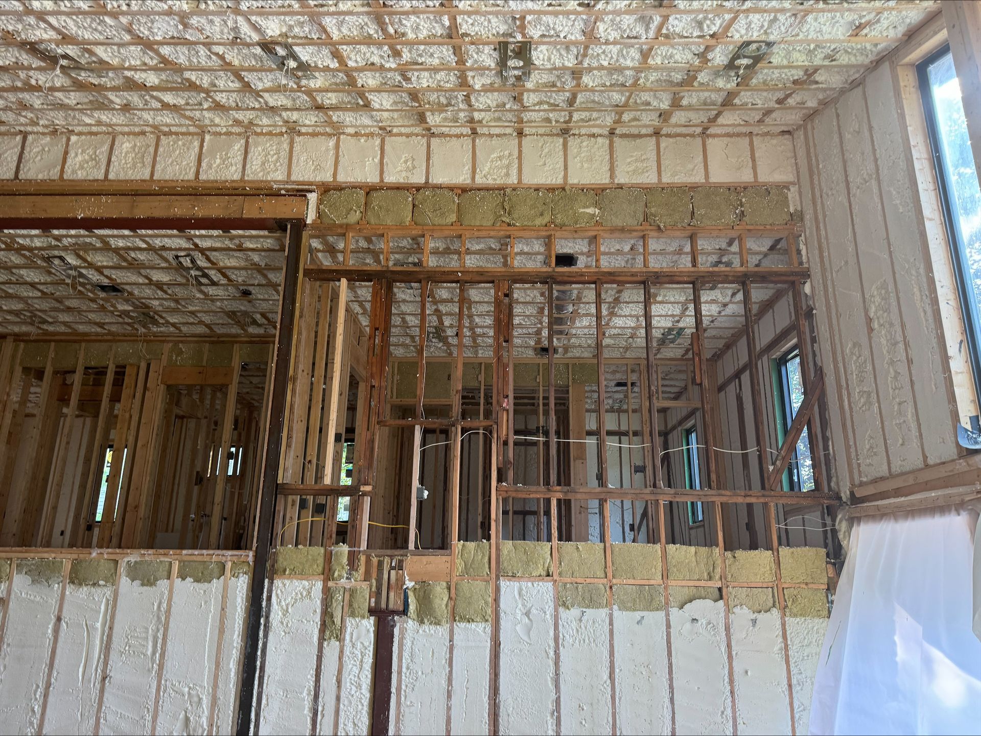 Interior of a building under construction with exposed wooden framing, insulation, and unfinished walls.