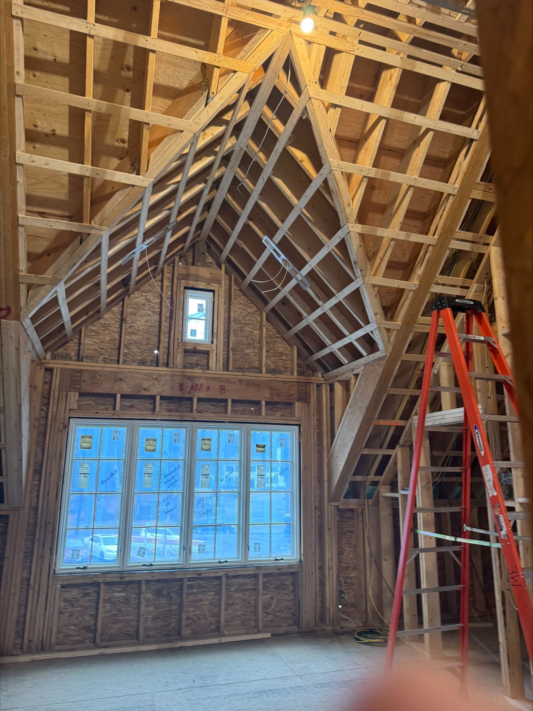 Attic room under construction with exposed rafters, blue-covered windows, and a red ladder.