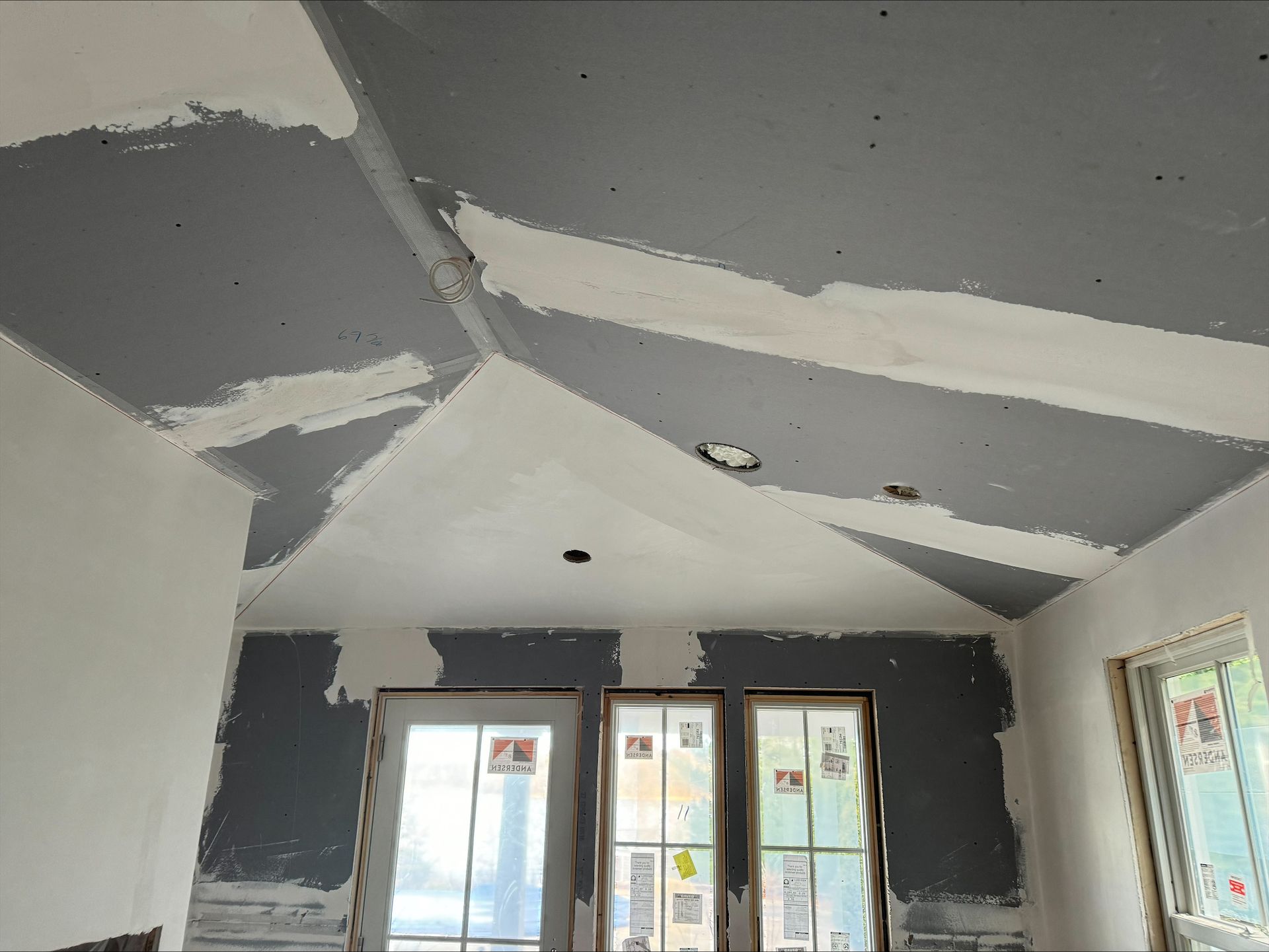 Damaged room ceiling with peeling drywall and two windows on the far wall.