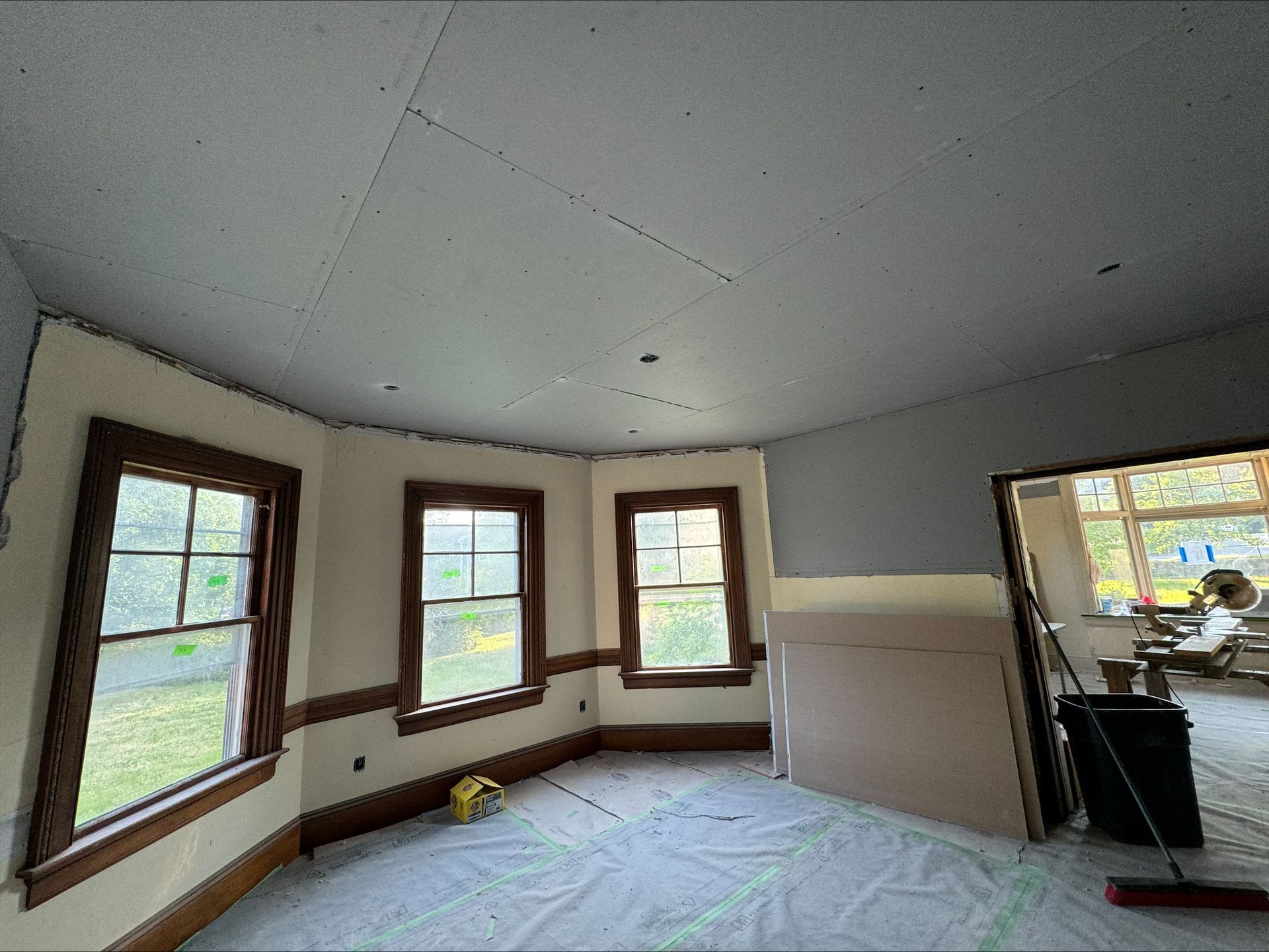 Empty room under renovation with bare drywall, three windows, and construction materials on the floor