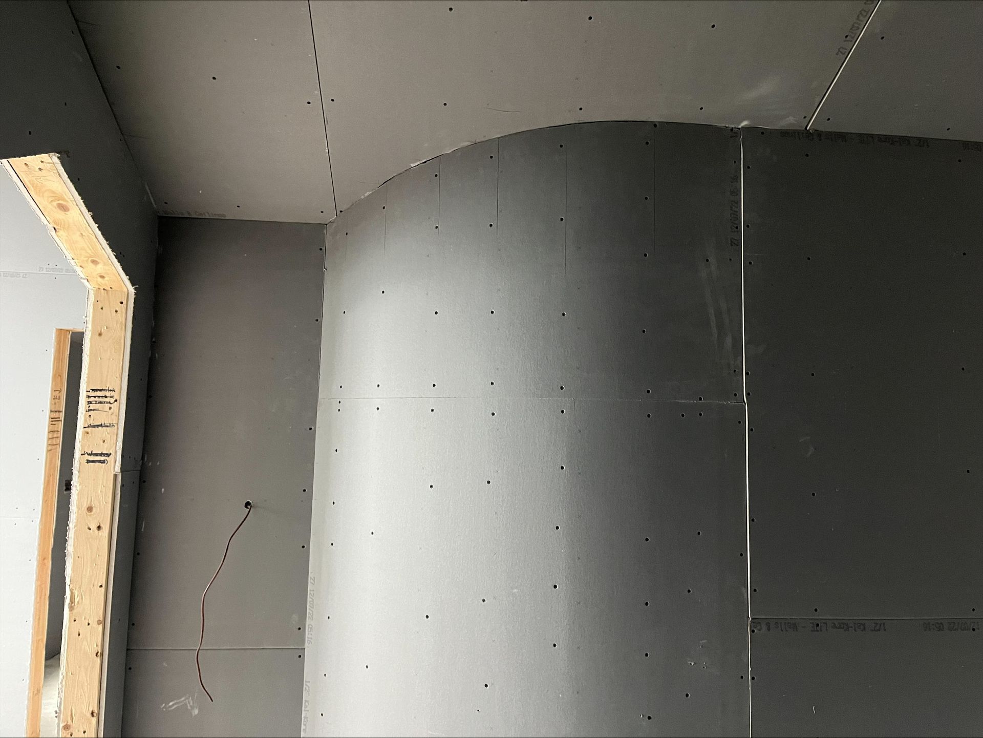 Unfinished interior wall with gray drywall and exposed framing near a doorway