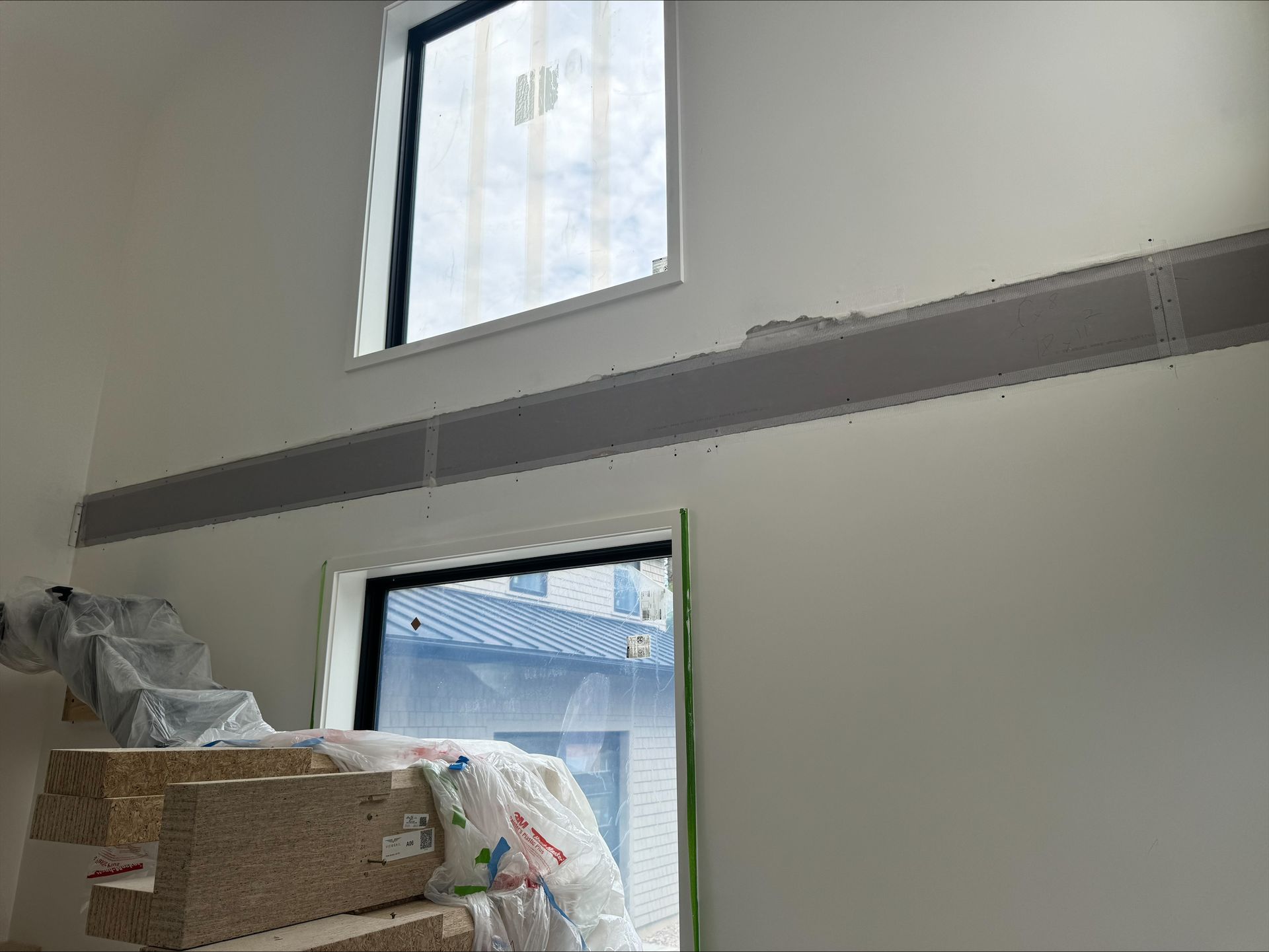 Sparse room with two windows and a long wall-mounted shelf, boxes piled in the corner
