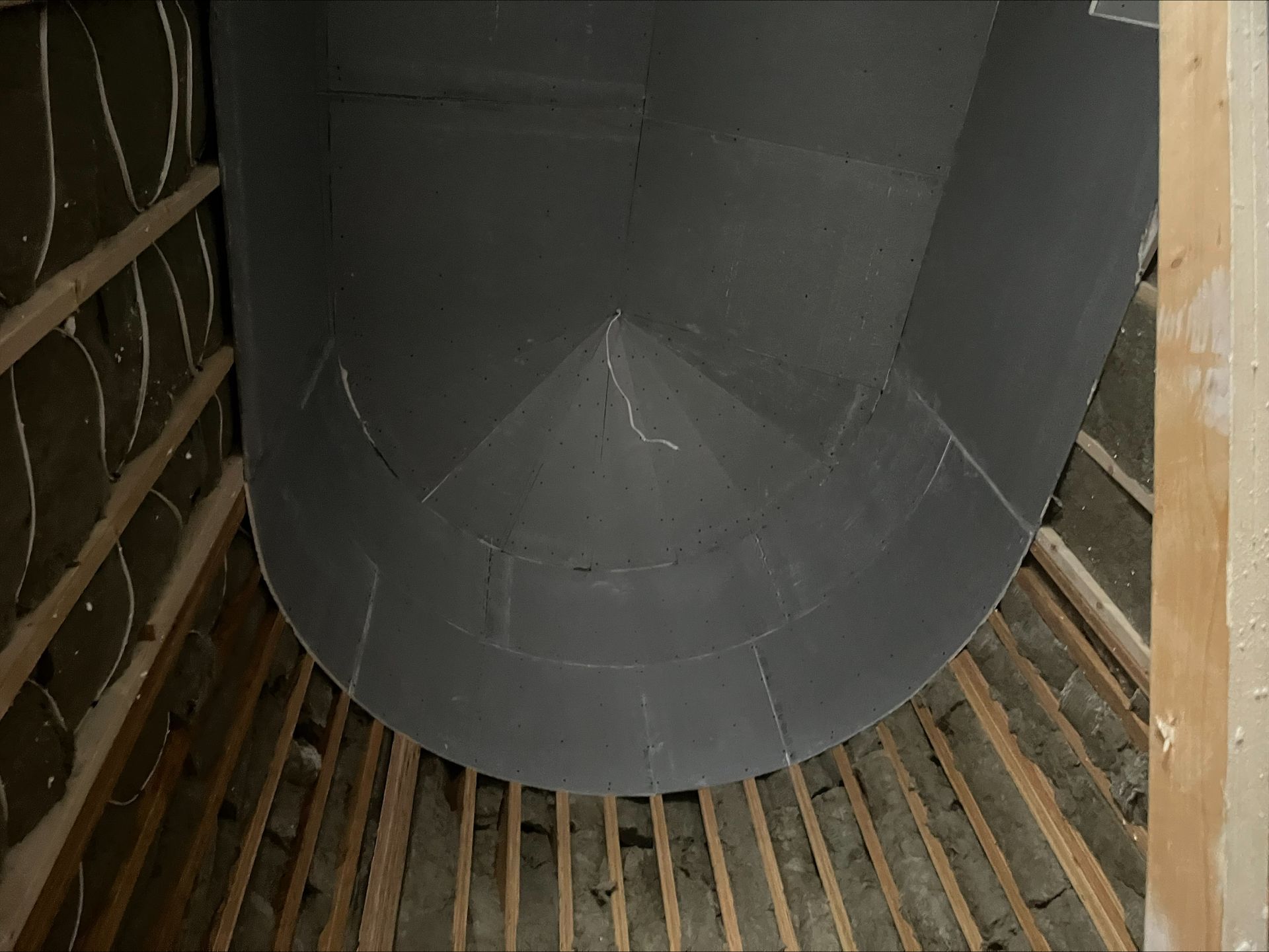 Large gray cylindrical tank inside a wooden-framed structure, viewed from below.