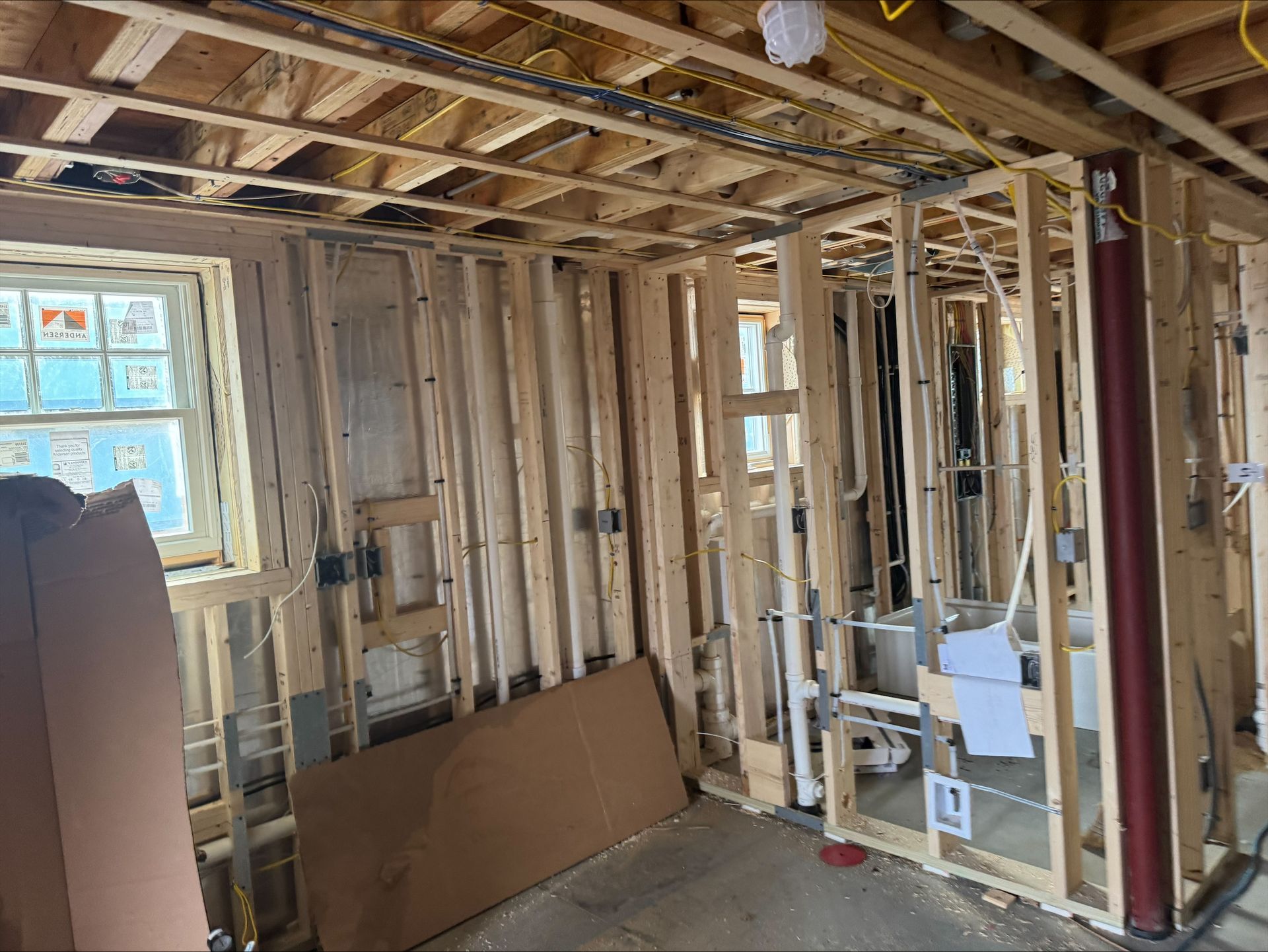 Partially renovated room with exposed studs, ceiling joists, a window, and construction materials on the floor