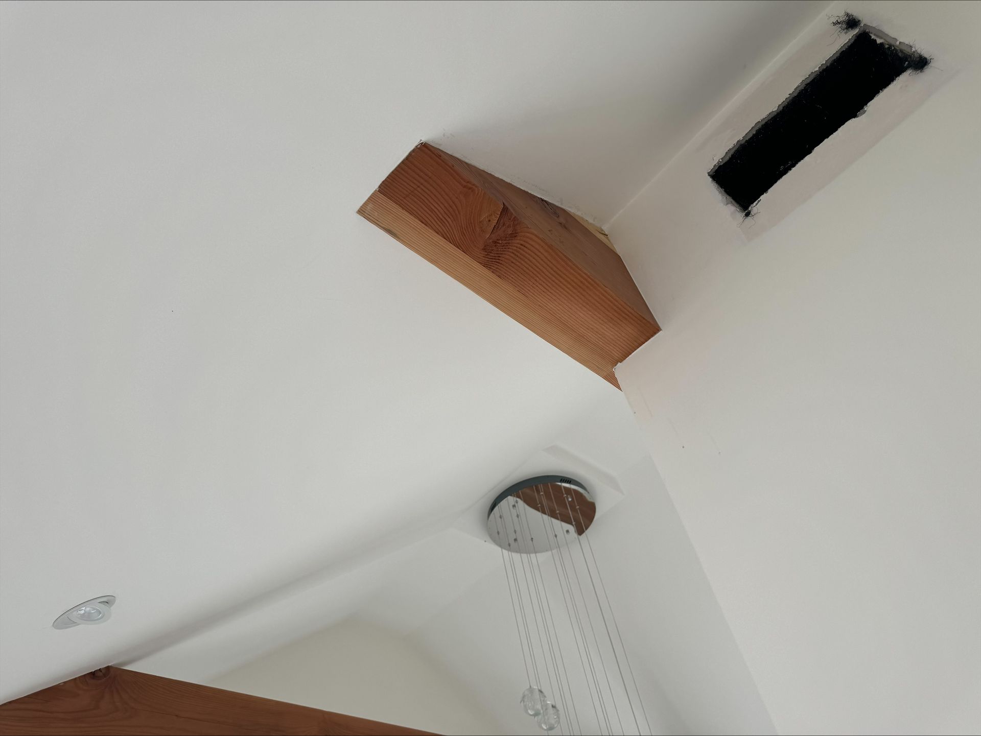 Ceiling with a wooden beam, recessed light, and shower head in a white bathroom
