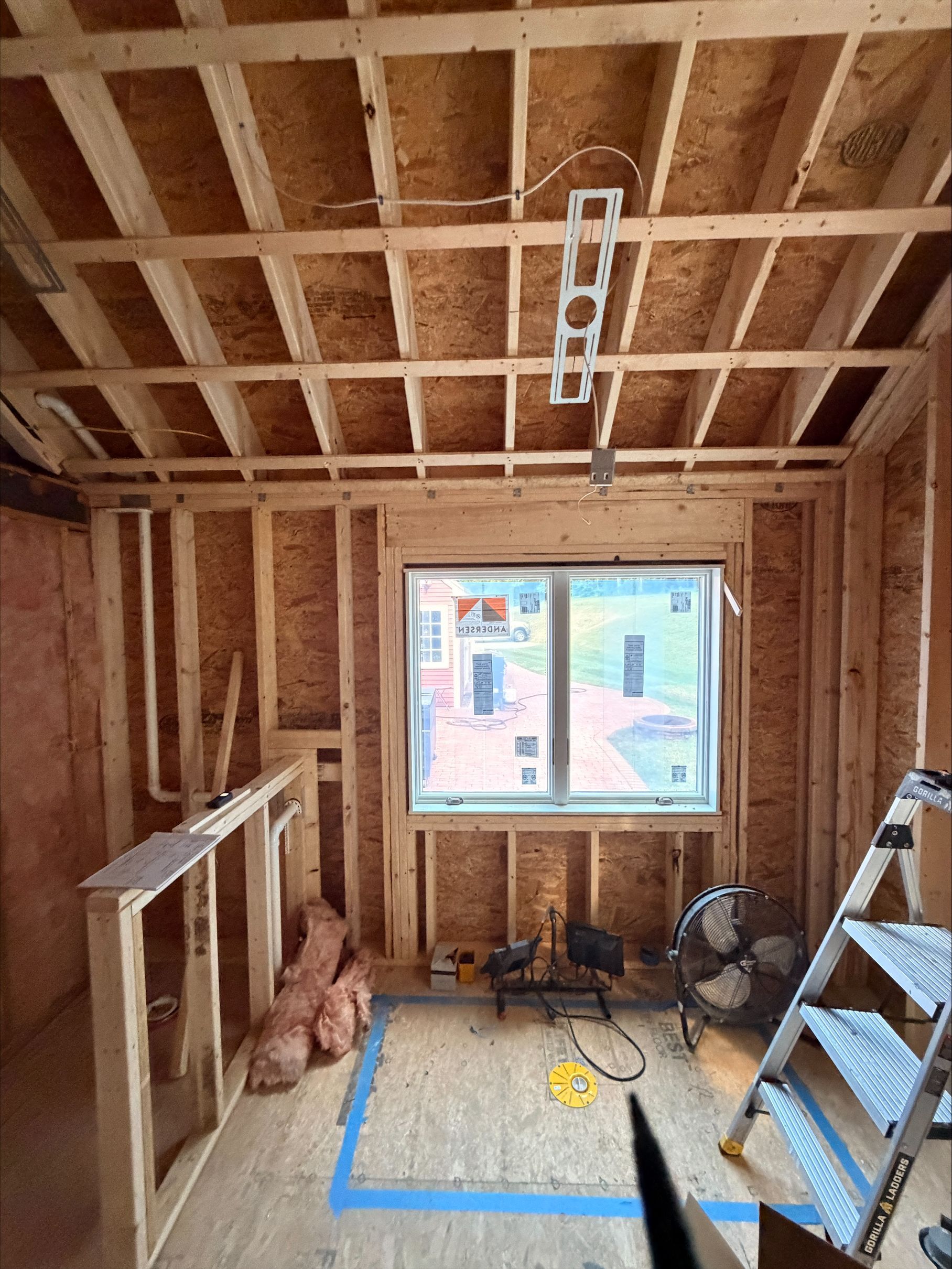 Unfinished room with exposed studs, window, ladder, and taped-off floor under construction