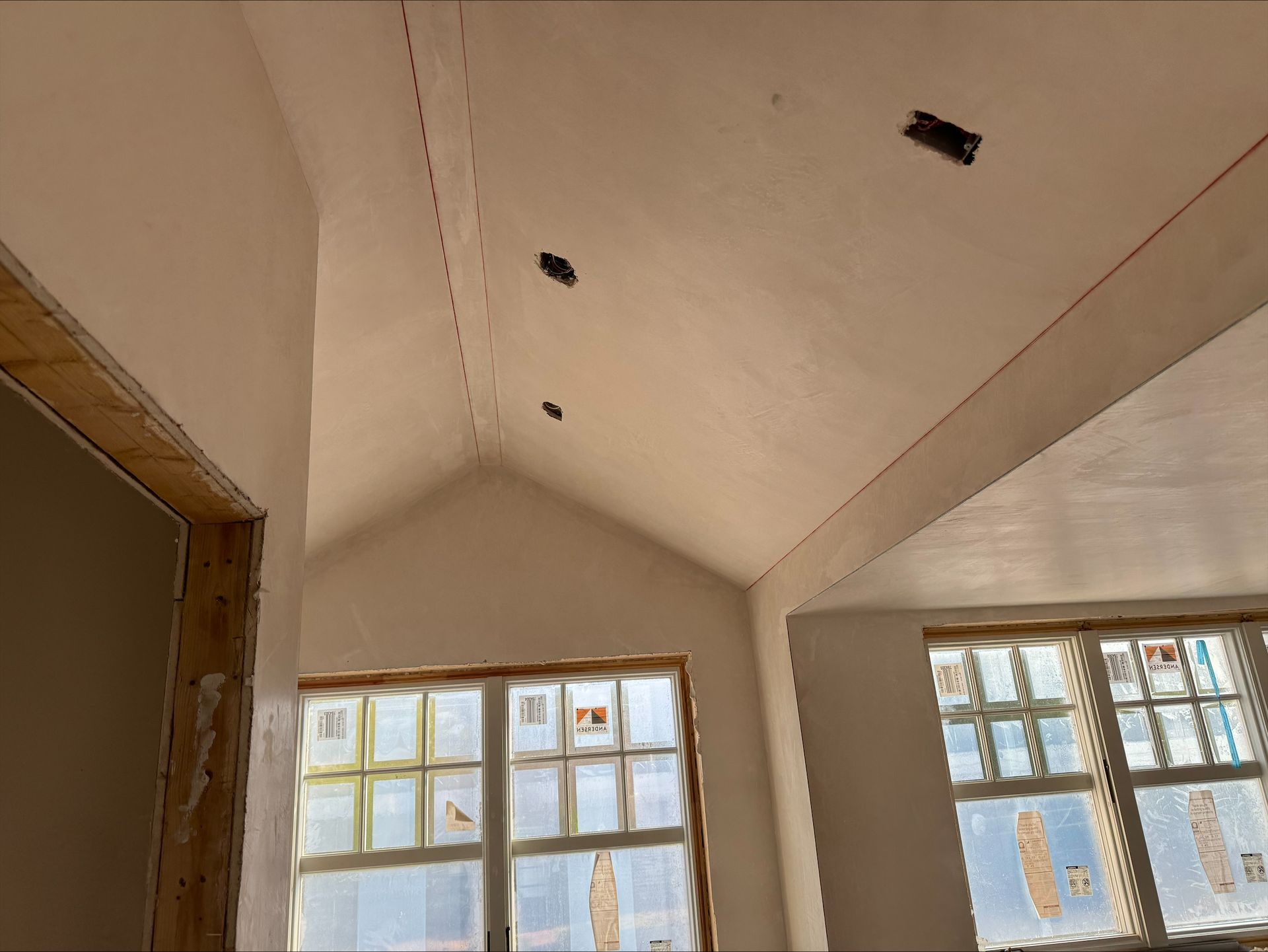 Renovation room with sloped ceiling, exposed openings, and large windows letting in daylight