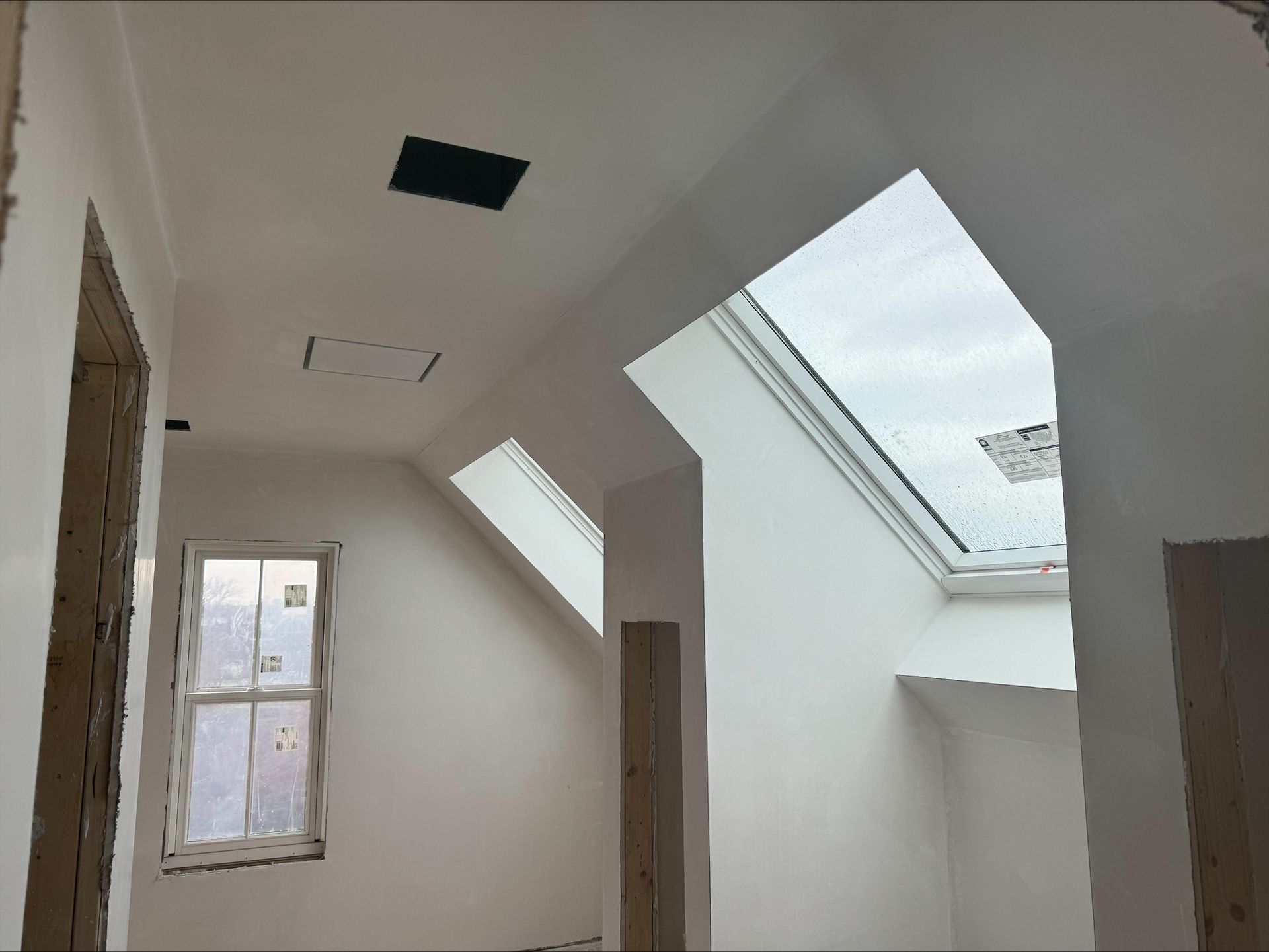 White unfinished attic room with slanted skylights and a small window, viewed from inside