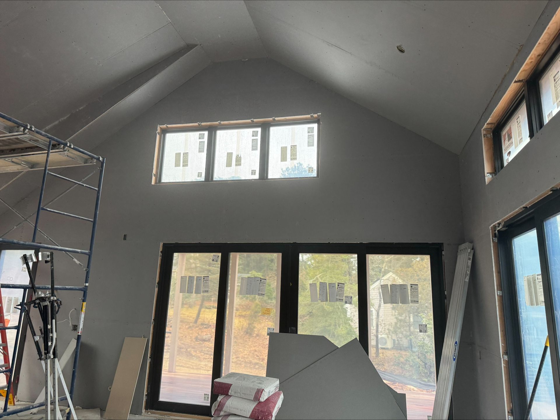 Unfinished room with gray walls, large windows, and construction materials stacked inside.