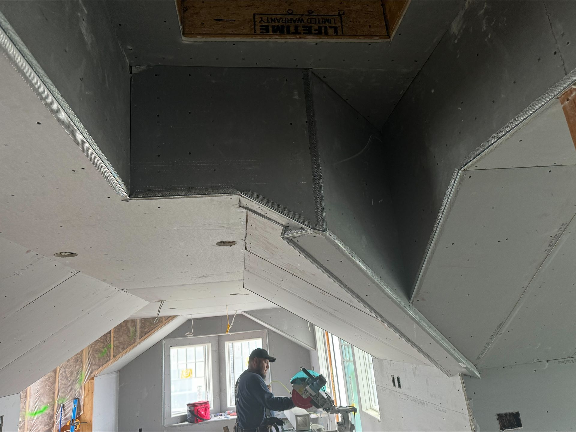 Exposed ceiling and walls in a room under renovation, with two workers below carrying materials.