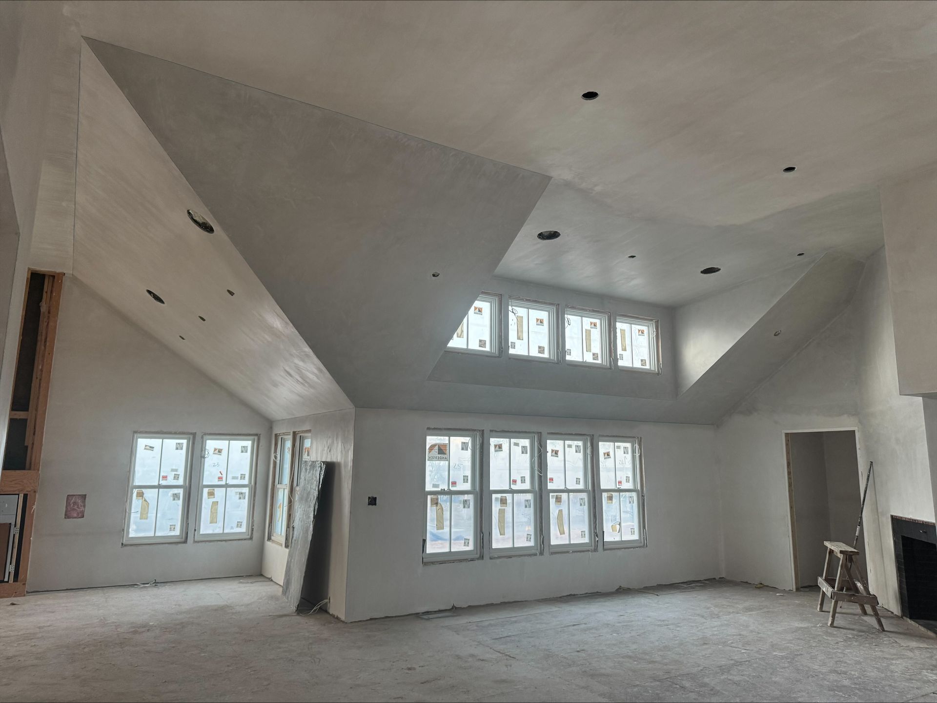 Empty unfinished room with white sloped ceiling and large windows letting in daylight