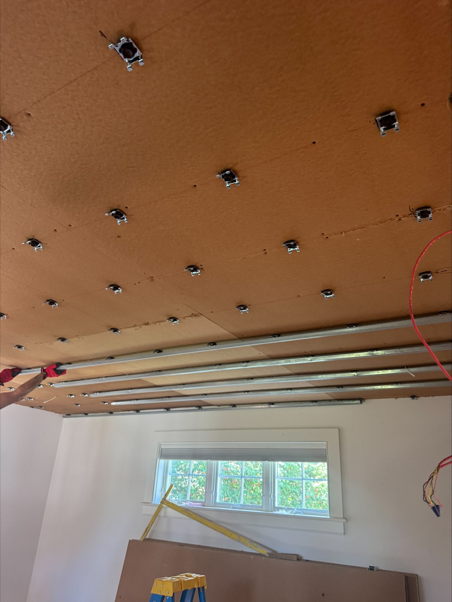 Unfinished room ceiling with orange panels, exposed wiring, and a small window on the back wall